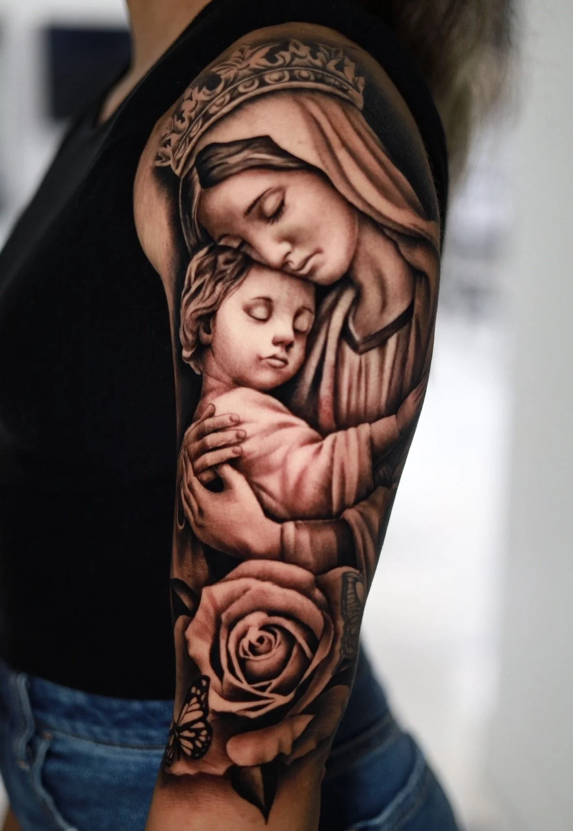 Tattoo of mother and child on arm with rose and butterfly details.