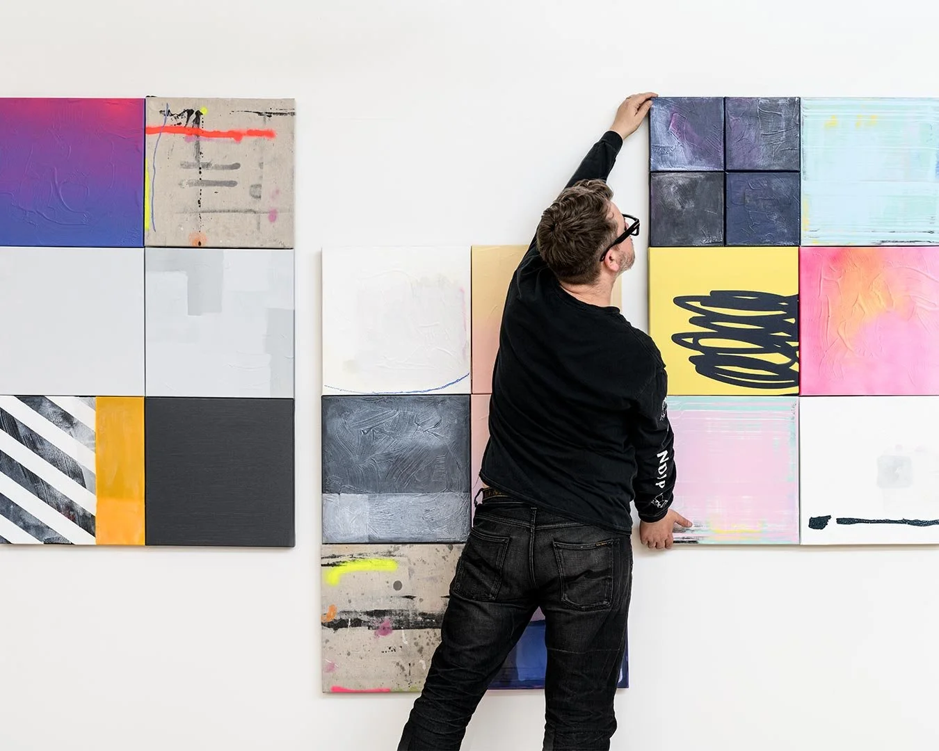 Christchurch, New Zealand artist, Nathan Ingram hanging a contemporary abstract painting on a white gallery wall.