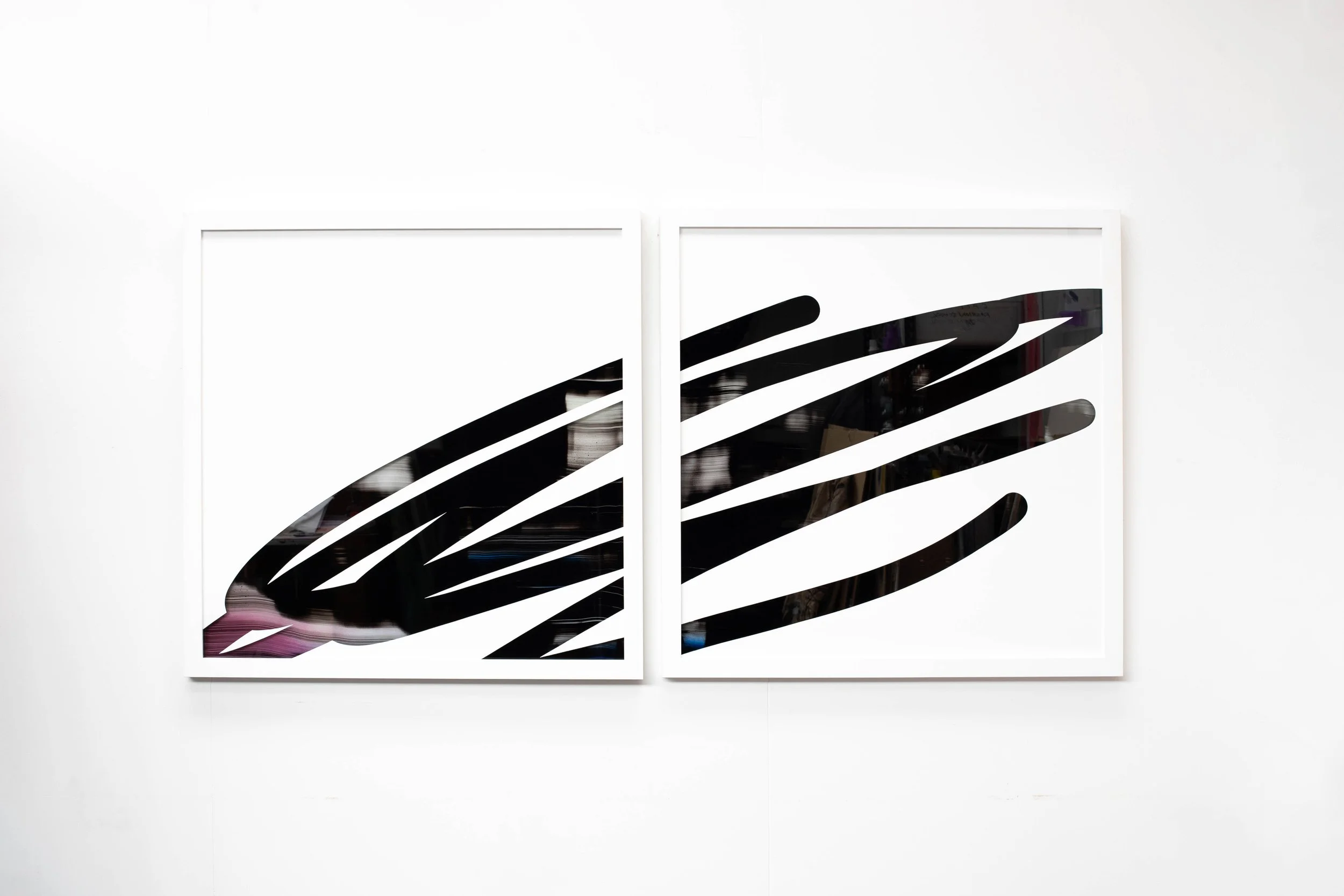 Two white-framed canvases with black abstract striped designs, hung side by side on a white wall.