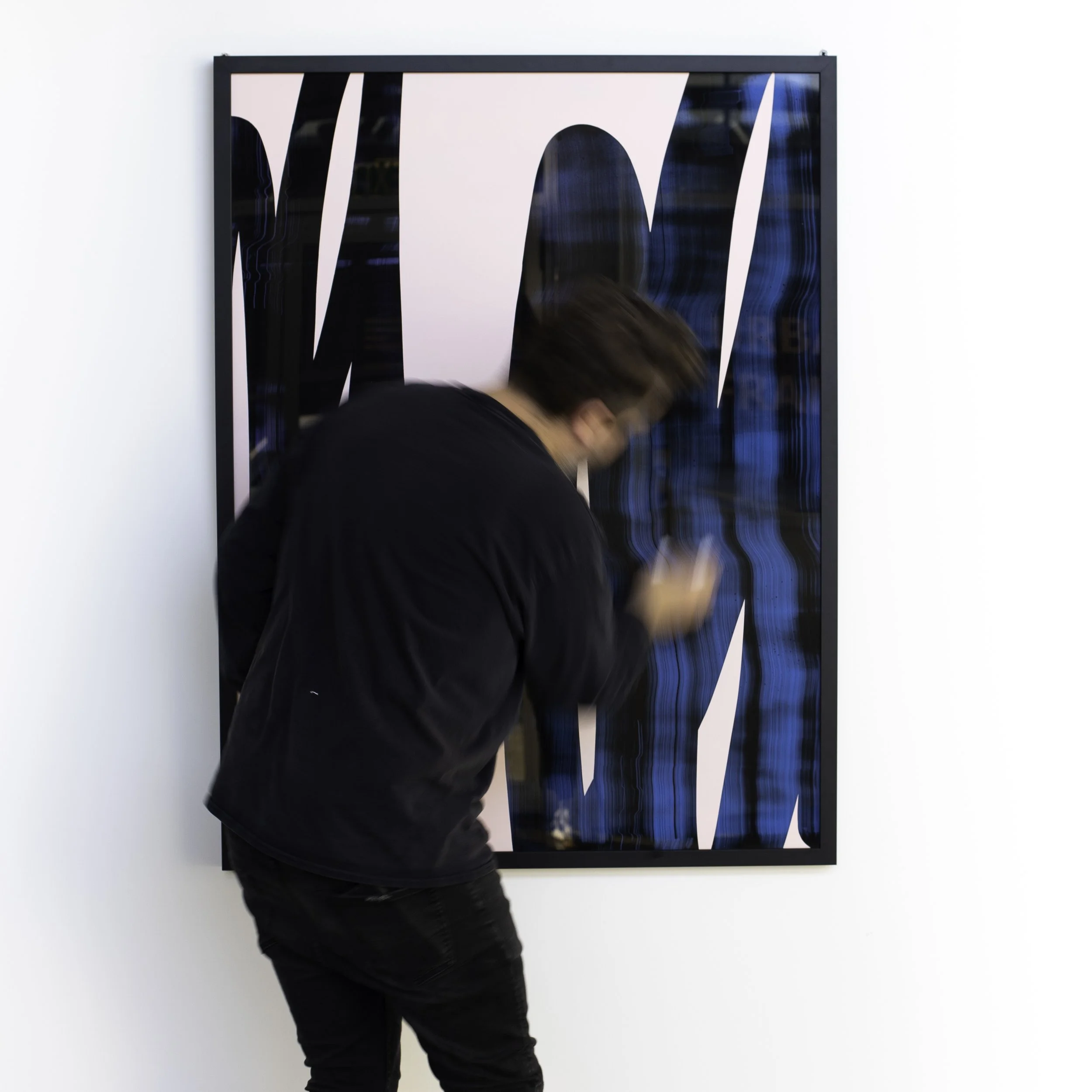 Person standing in front of a colorful abstract artwork on a white gallery wall, looking at their phone.