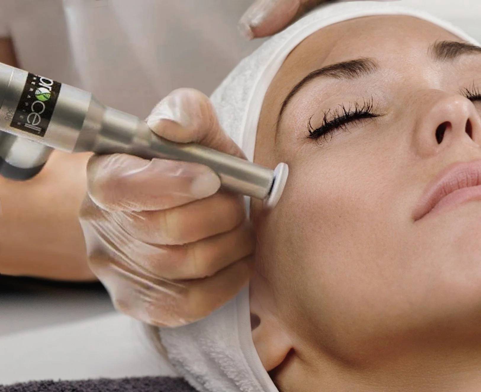 A woman receiving a facial treatment with a skincare device on her cheek at a spa or clinic.