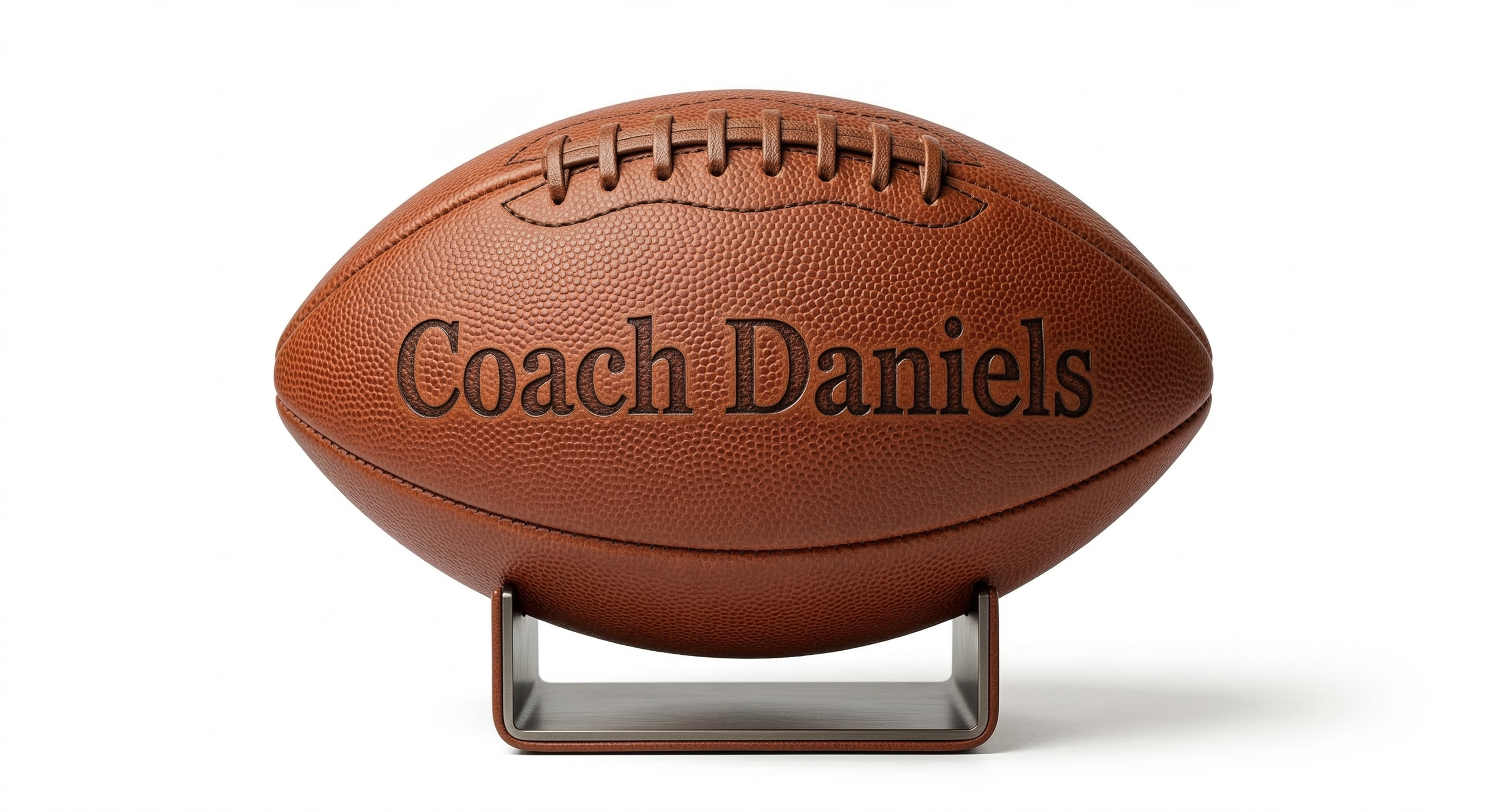 A brown American football with the name "Coach Daniels" engraved on it, displayed on a stand against a white background.