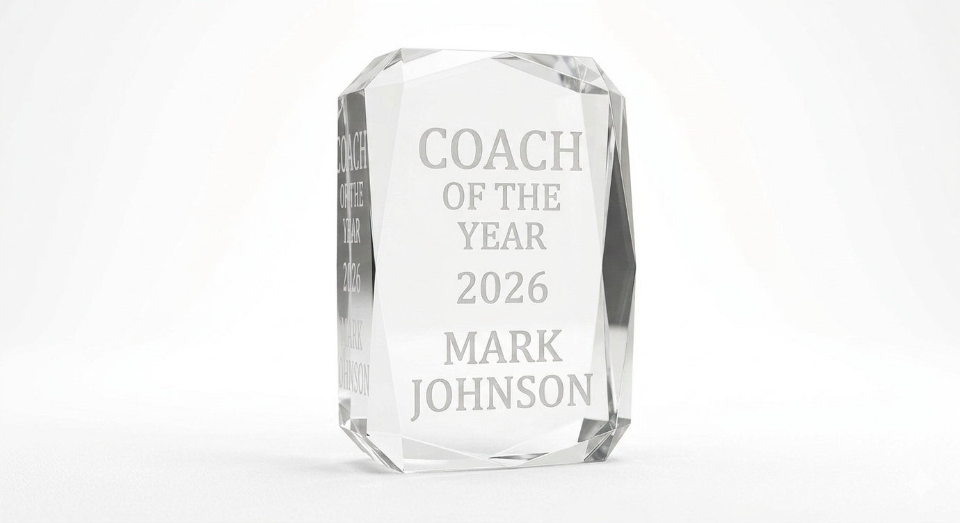 A clear crystal award with the inscription 'Coach of the Year 2026 Mark Johnson' engraved on it.