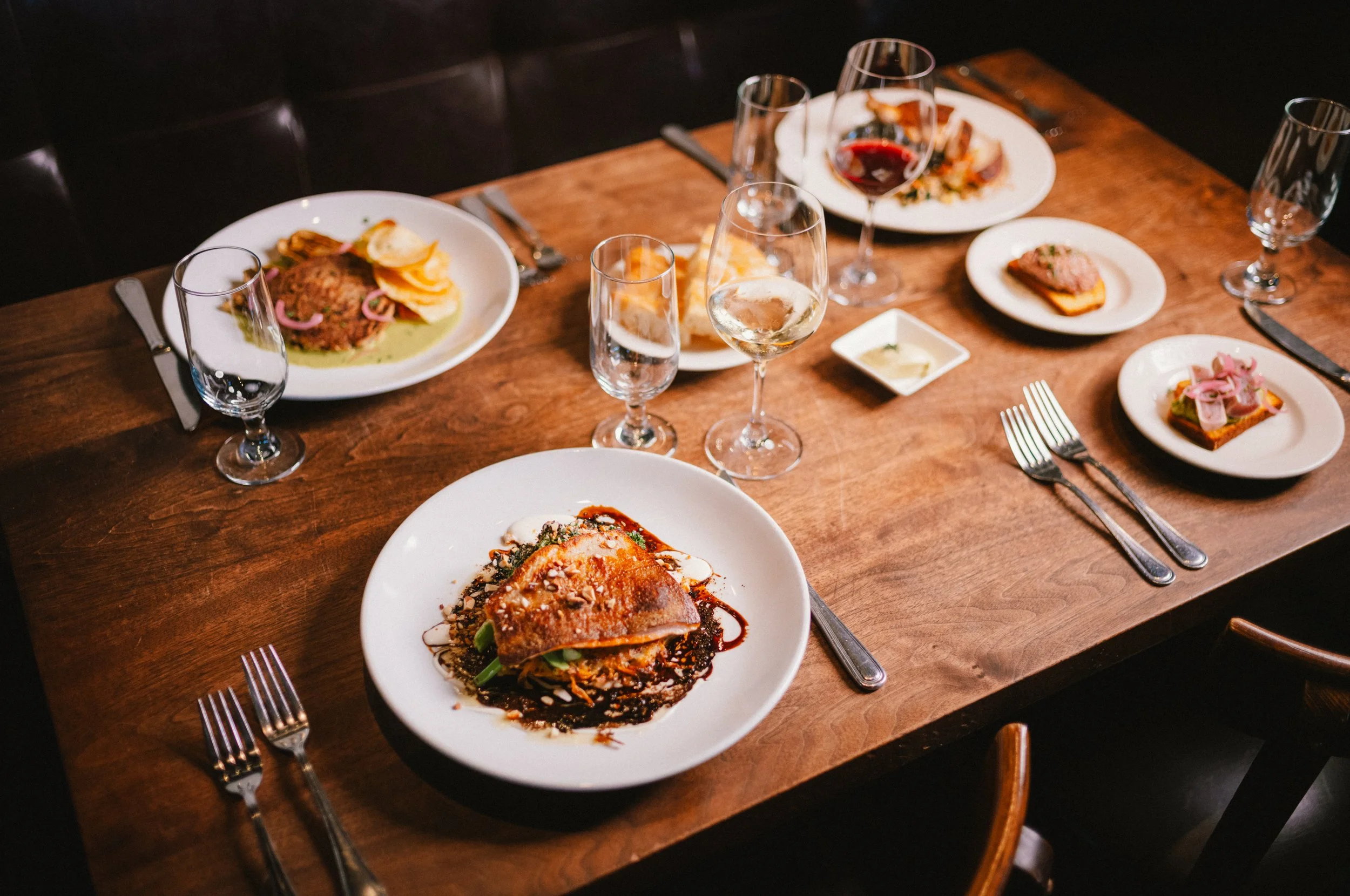 A rustic dining table set with multiple plates of gourmet food, wine glasses, and silverware, ready for a meal.