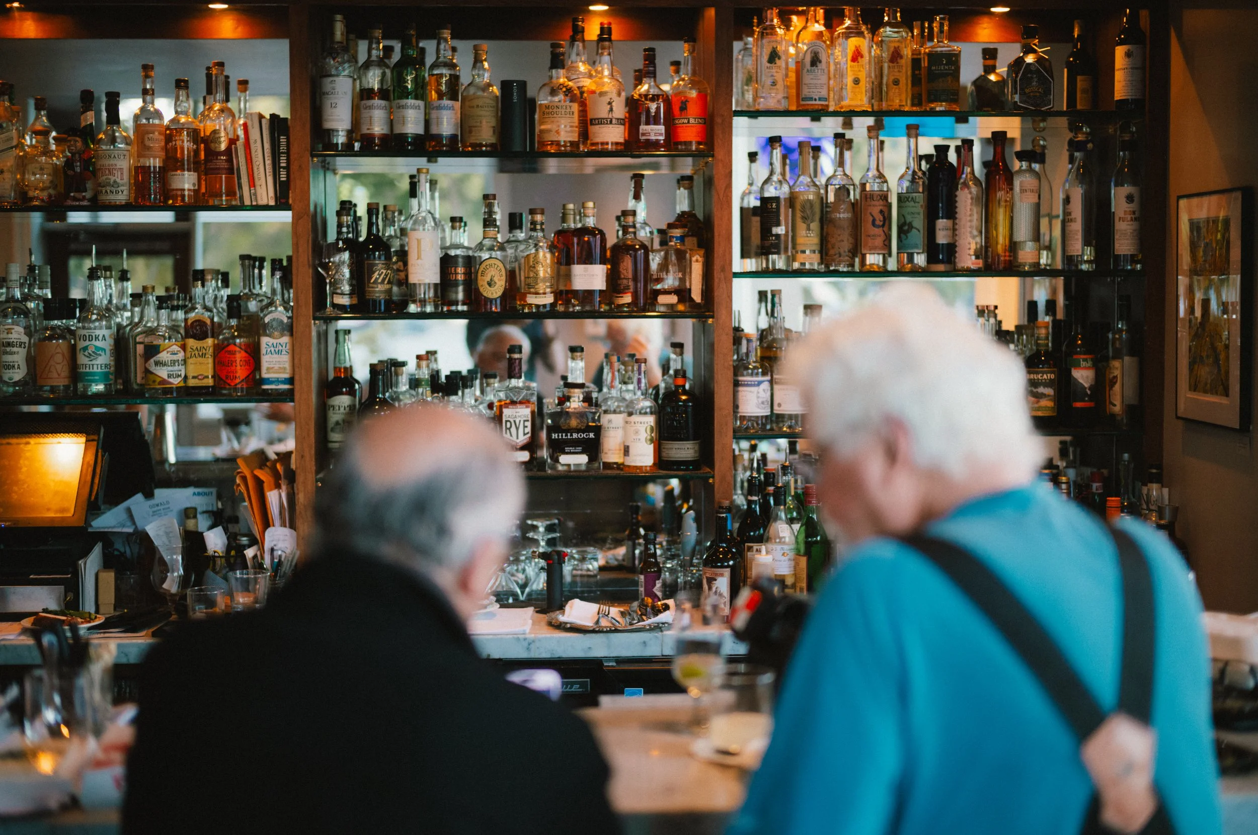 People sitting at a bar with shelves of various liquor bottles behind them.