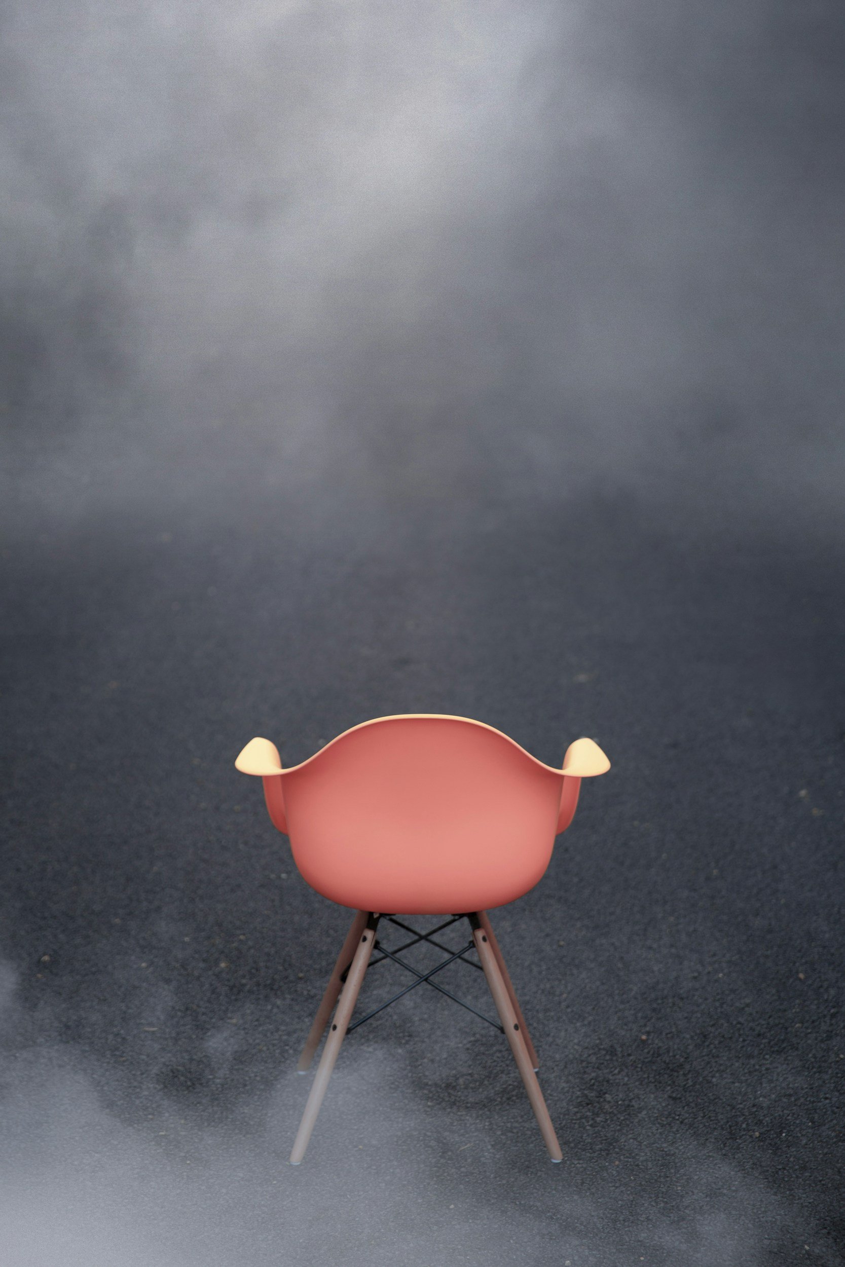 Pink chair with wooden legs on a dark, cloudy outdoor background.