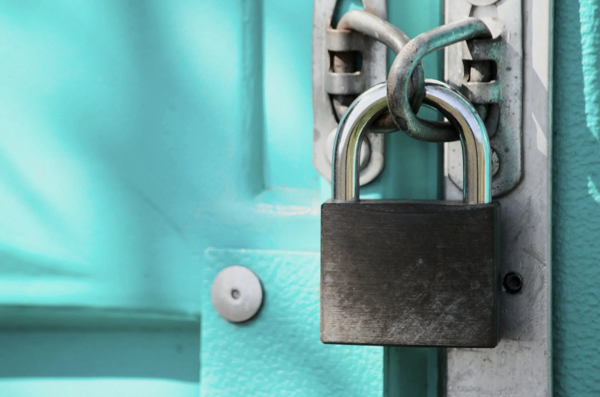 A black padlock securing a metal latch on a door painted in turquoise.