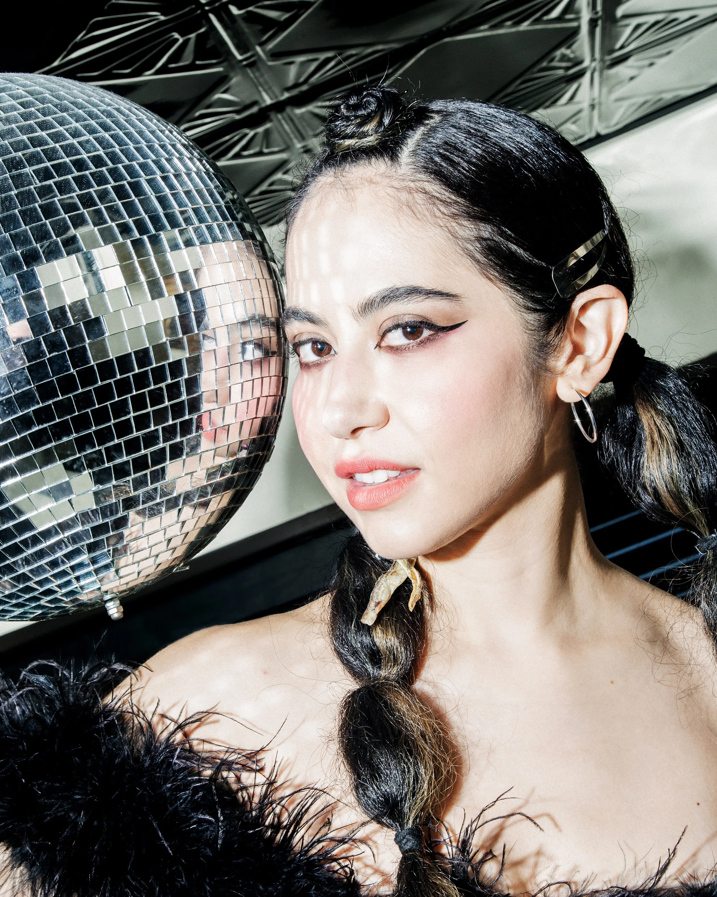 Shallowhalo, Brooklyn-based DJ and synth pop artist, posing beside a disco ball in a black feathered outfit.