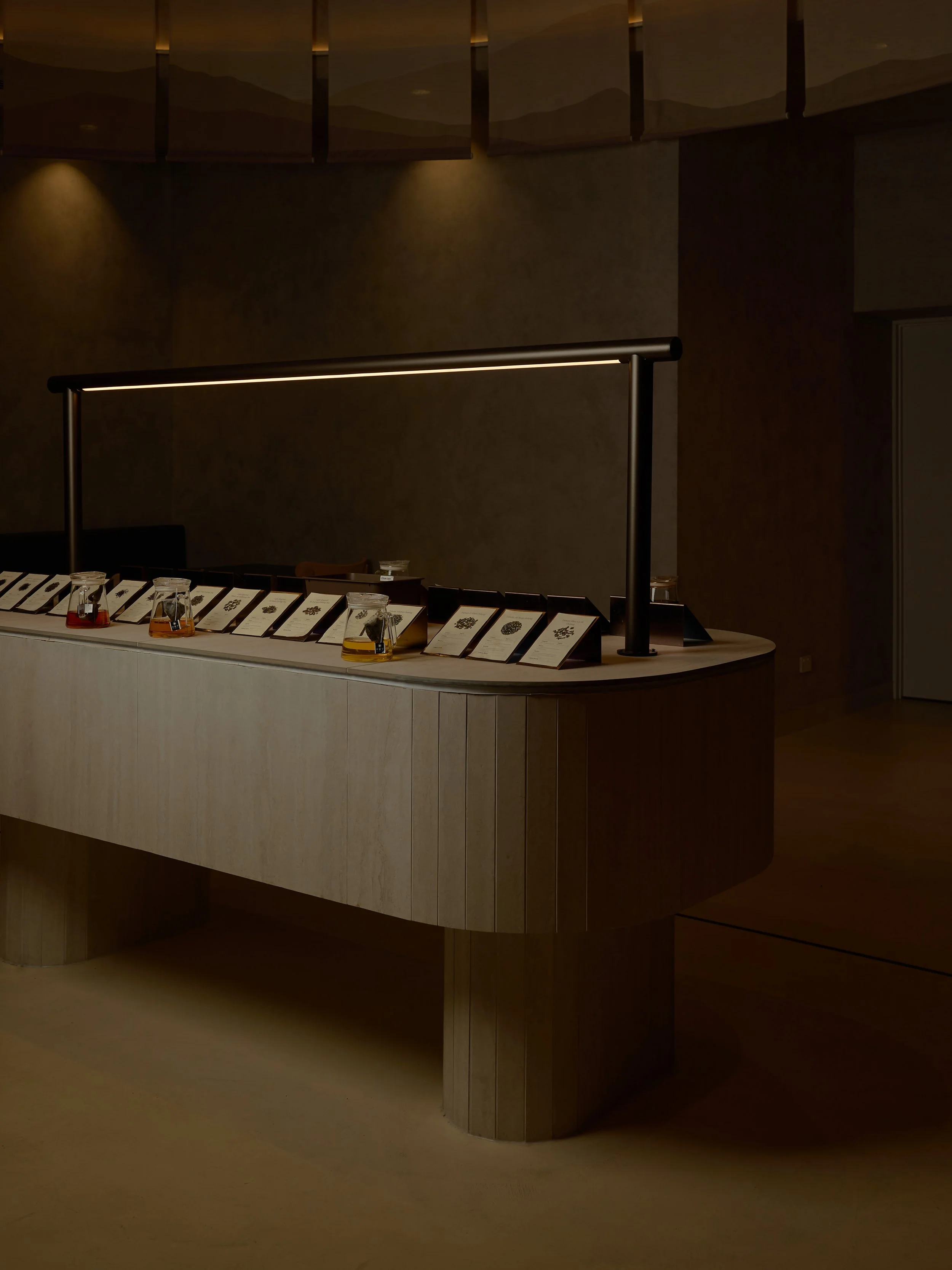 A display counter with informational placards and small jars containing various colored ingredients or objects, under a modern black light fixture, in a dimly lit room.