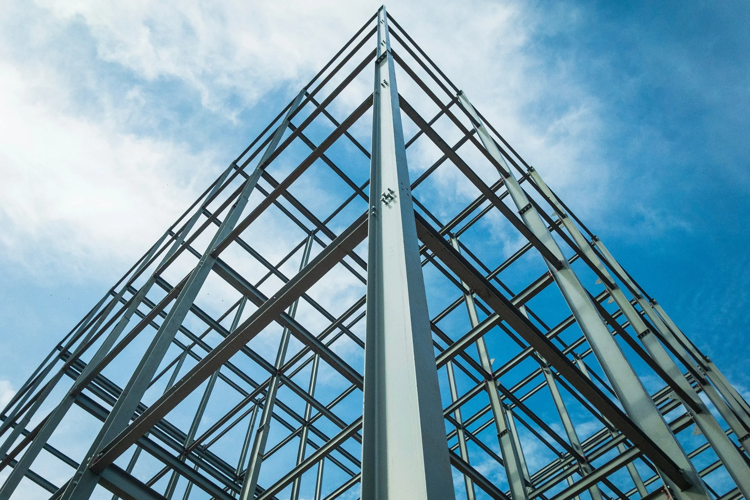 Low-angle view of a steel frame building structure against a partly cloudy sky.