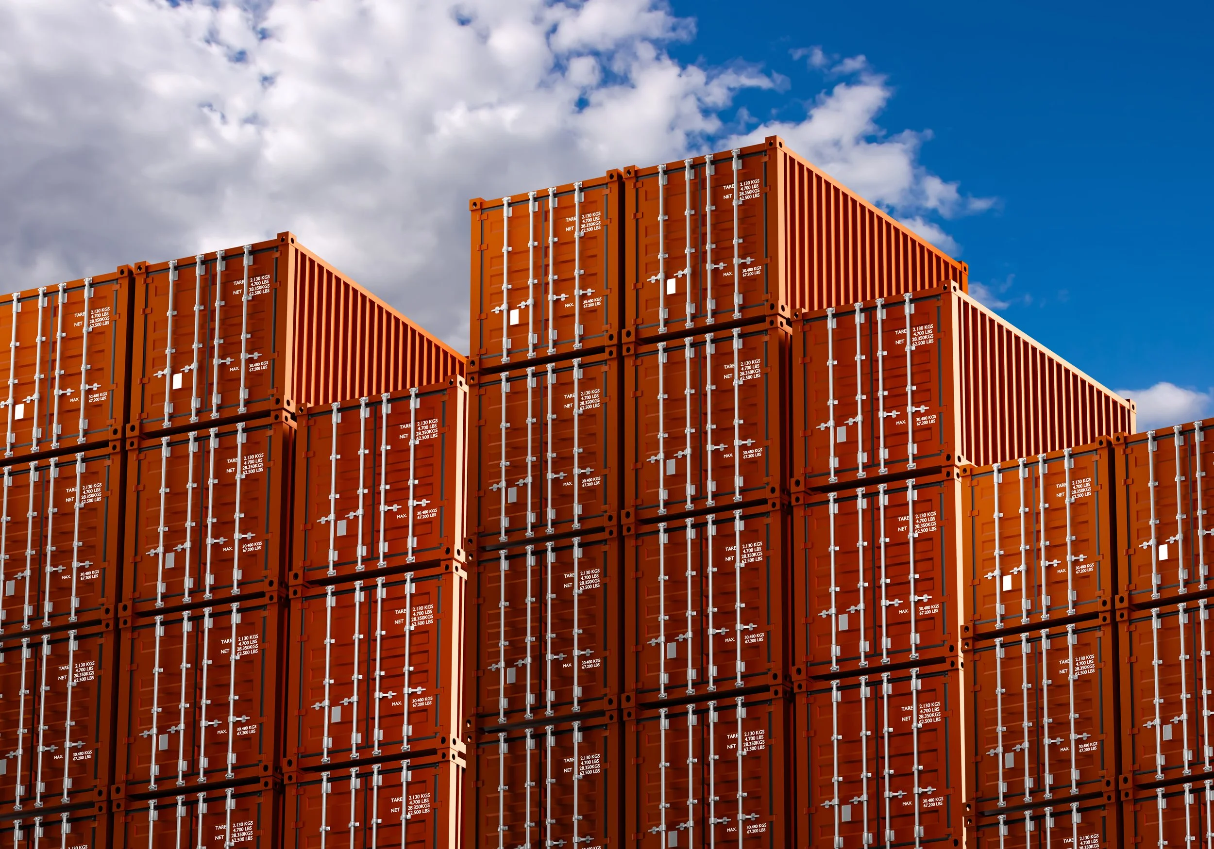 Multiple orange shipping containers stacked outdoors against a blue sky with clouds.