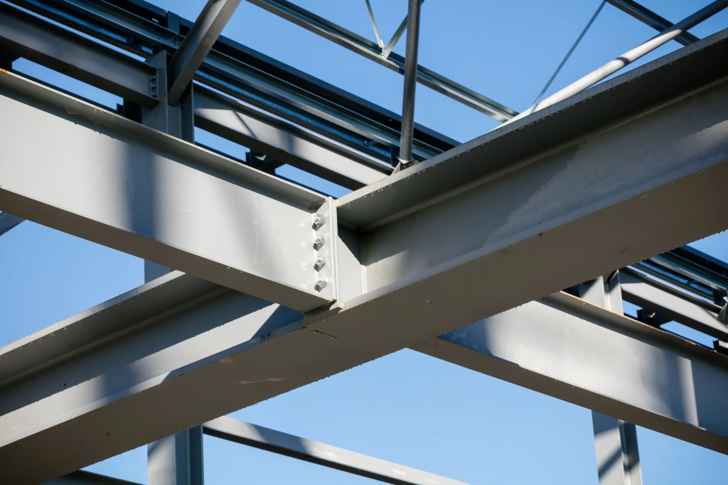 Close-up of a metal industrial structure with beams, bolts, and supports against a clear blue sky.