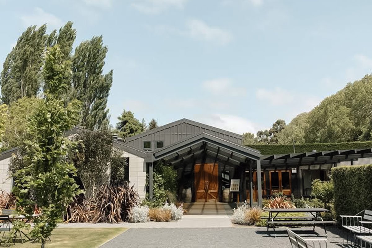 A modern house with a large open entryway, surrounded by greenery and outdoor seating areas.