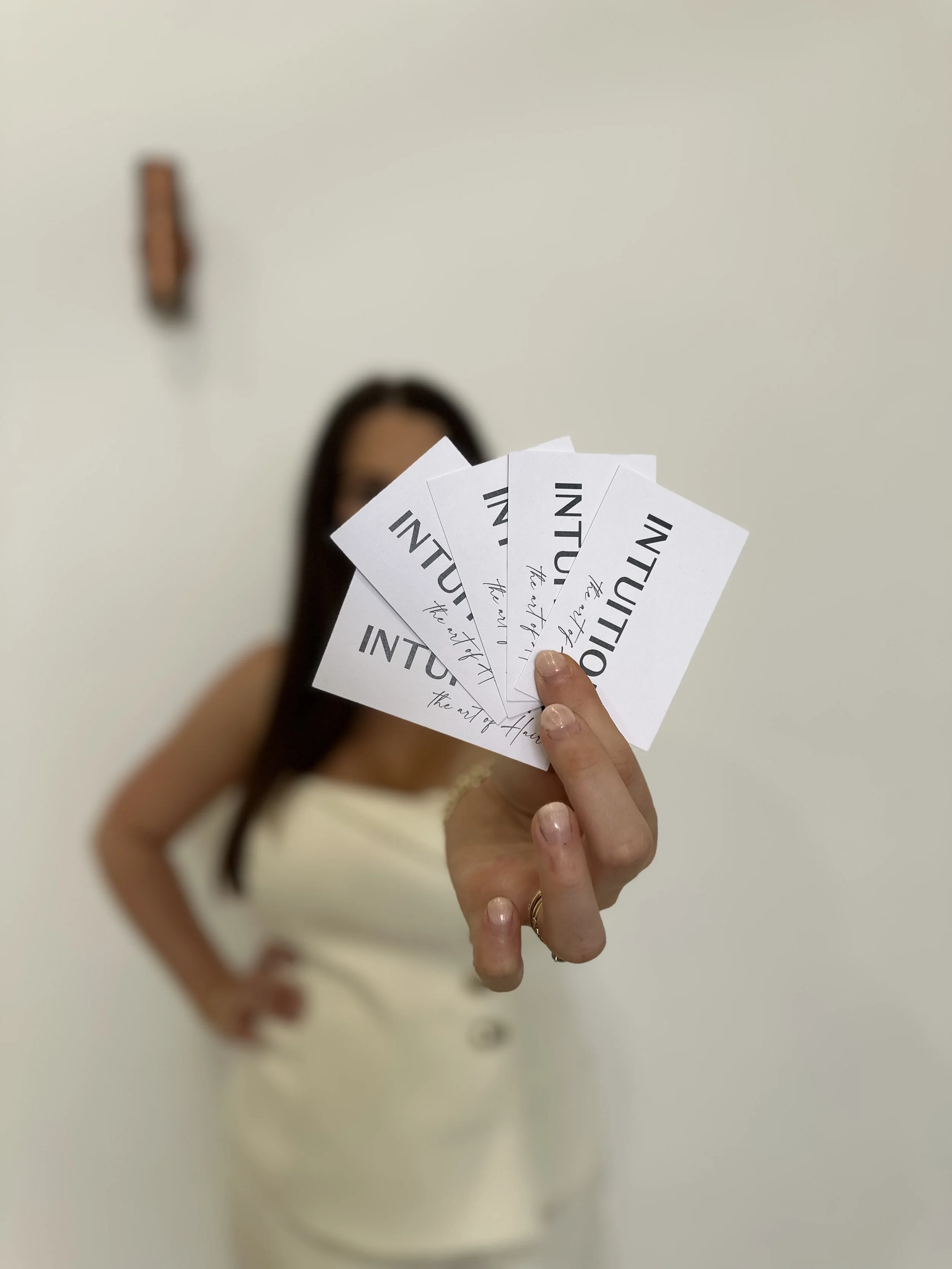 A person holding several white business cards with the words "INITIATION" and handwritten text, blurred background showing a woman in a white dress.