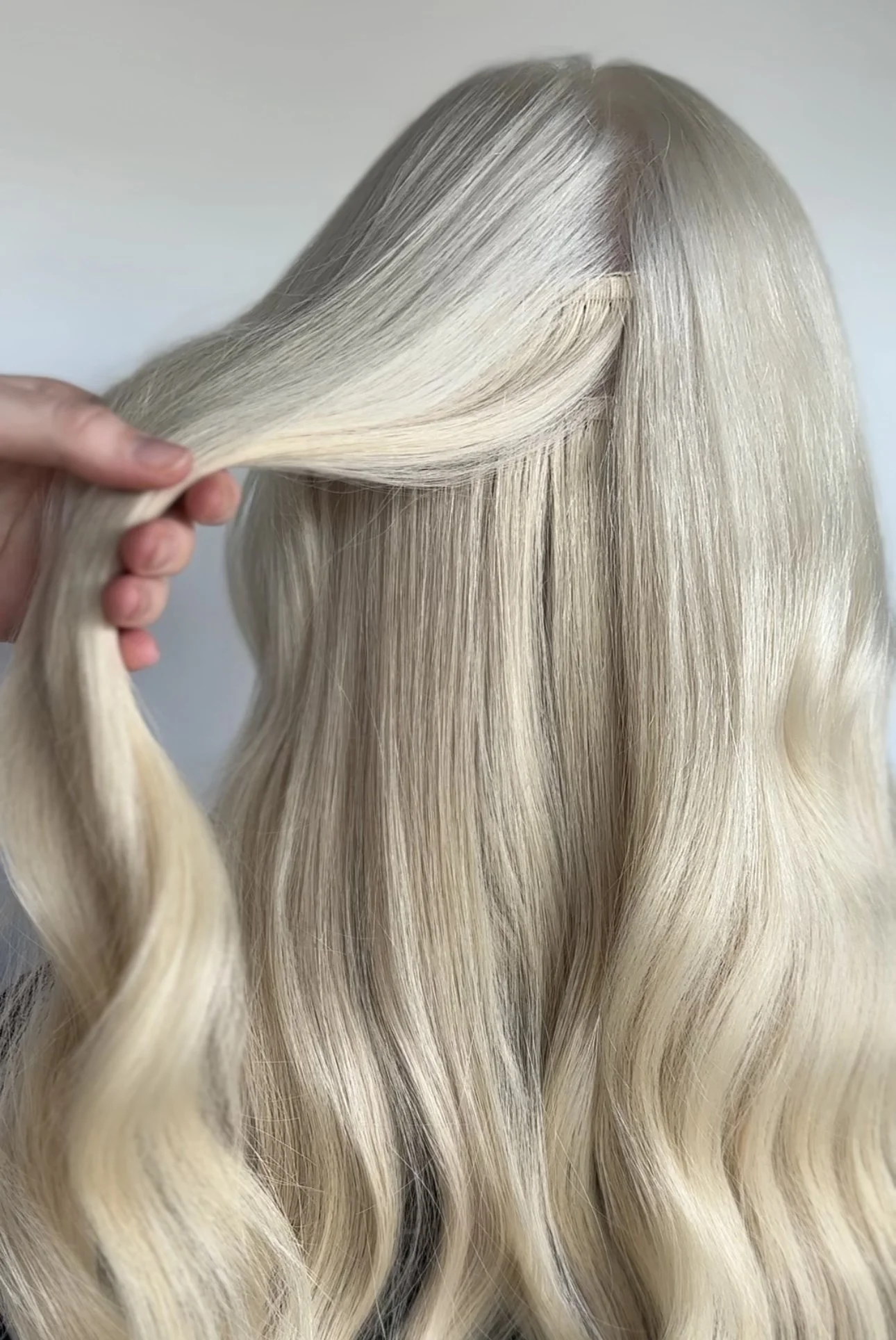 A close-up of long, wavy blonde hair being held and styled.