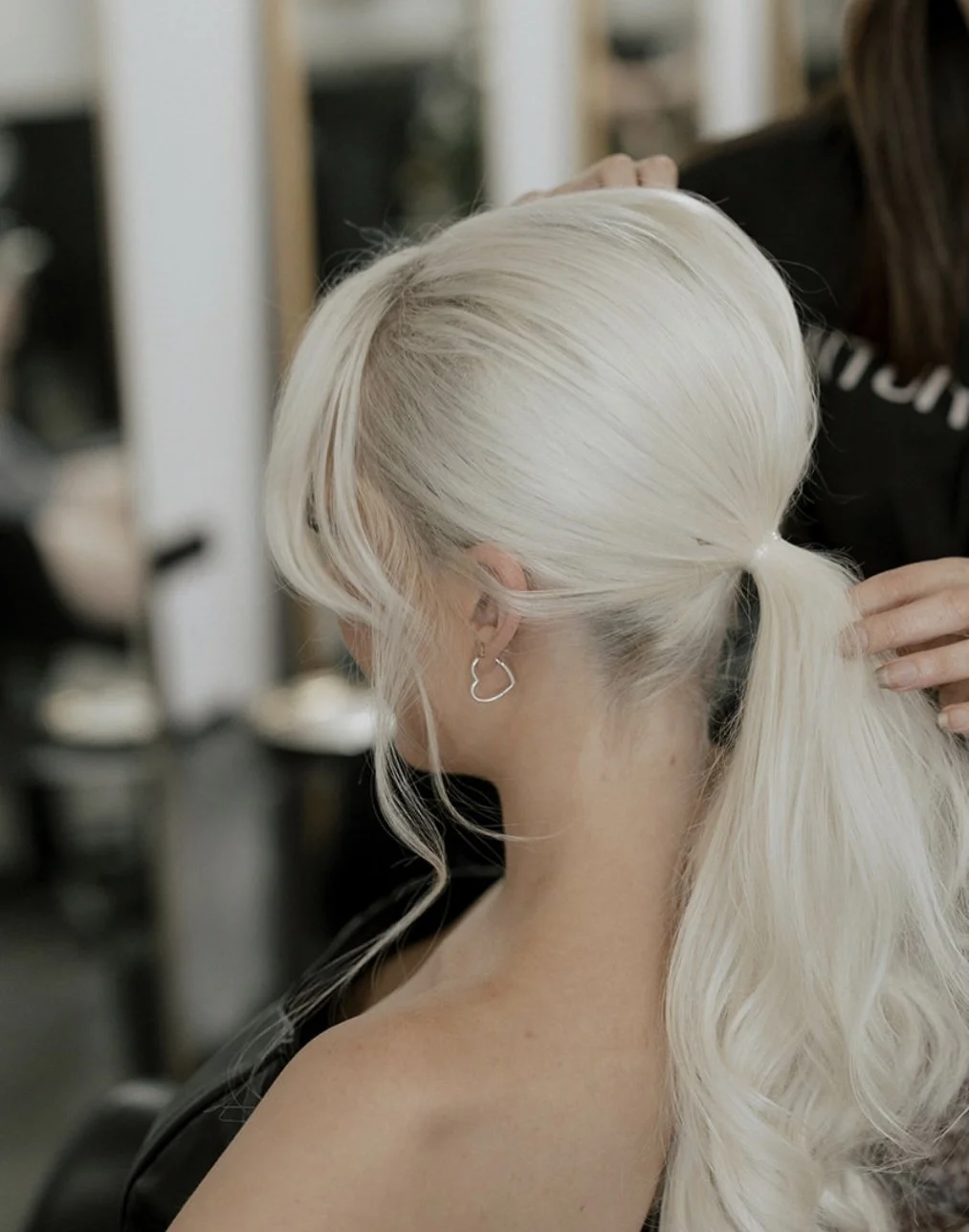 A woman with platinum blonde hair in a ponytail having her hair styled at a salon.