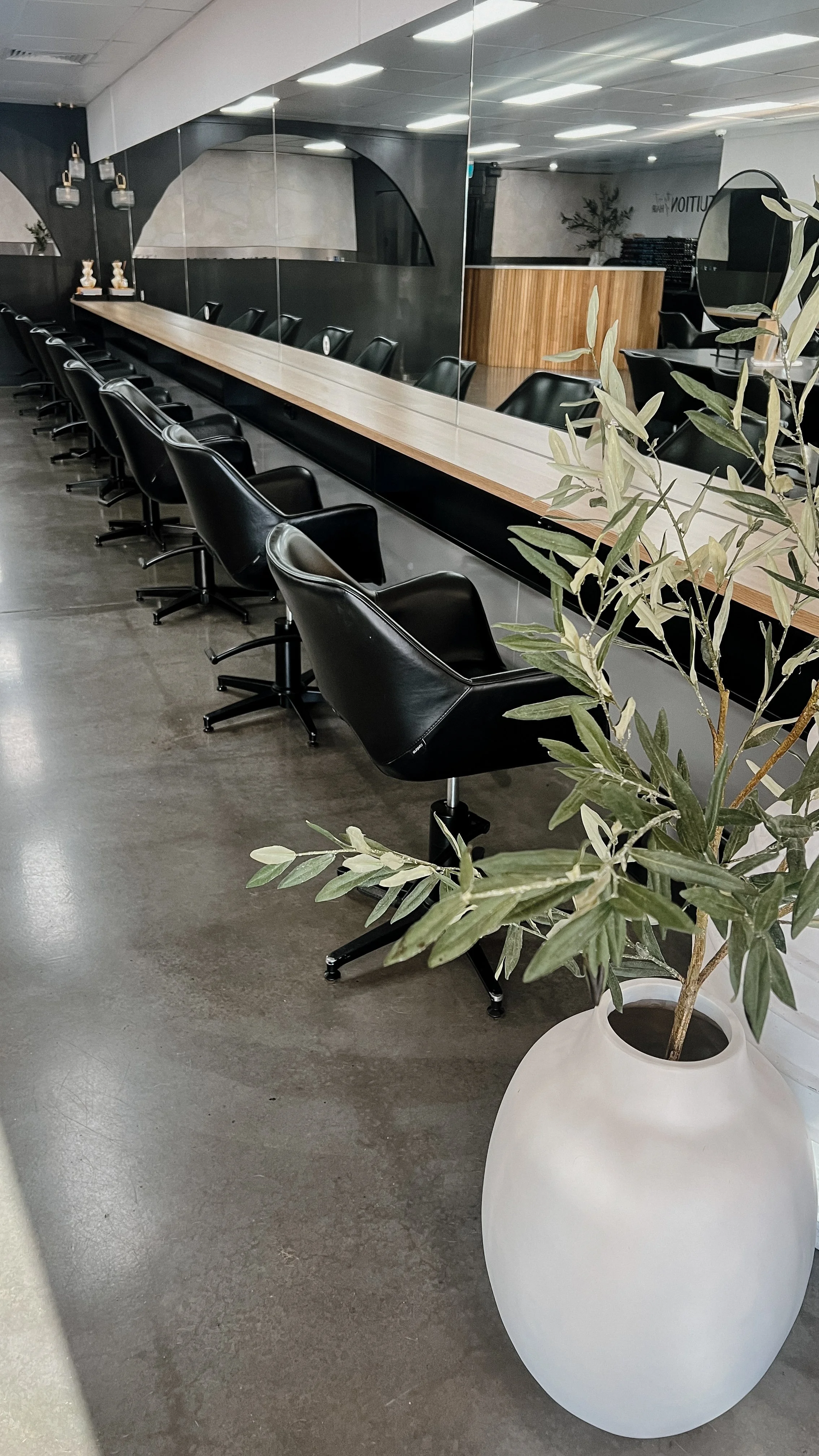 A modern conference room with black leather chairs along a long wooden table and a large mirror on the wall. There is a potted plant in a white vase in the foreground and decorative rabbit figurines on a shelf.