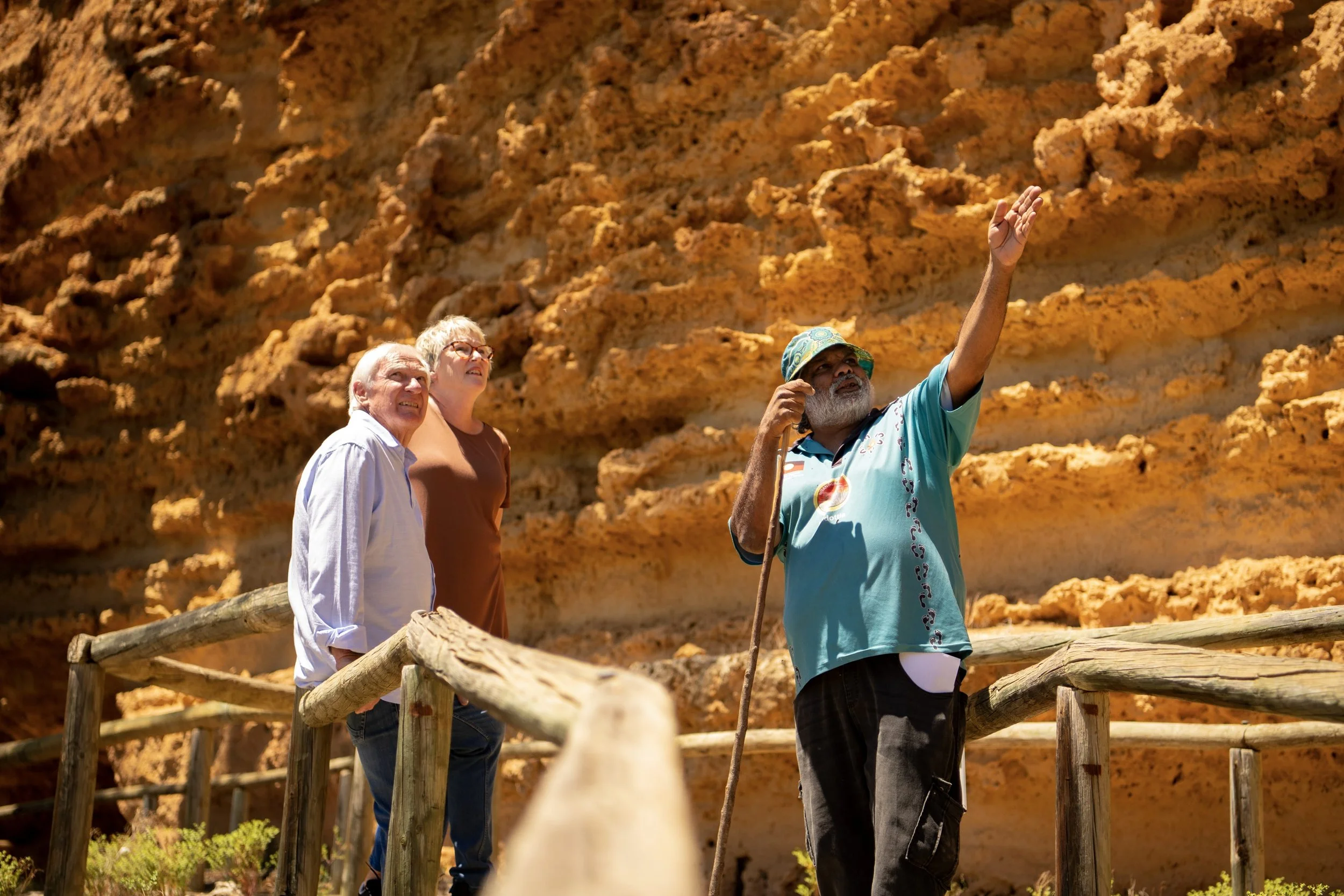 Guide showing tourists the rocks on a cliff, with two women and an older man listening and looking up, in a scenic outdoor area.