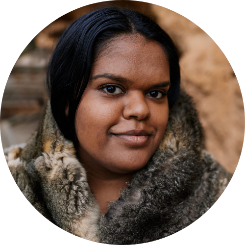 Close-up of a woman with dark hair and brown skin, wearing a faux fur coat, outdoors.