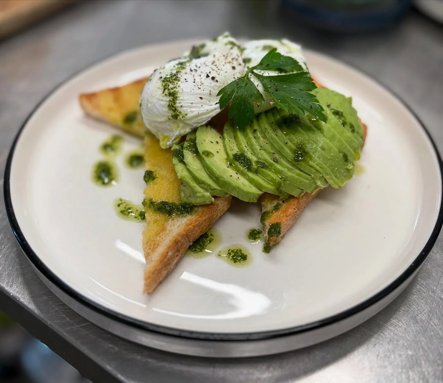 Bella's Avocado on toast with poached egg, mini hash browns, salsa, and cilantro on a white plate.
