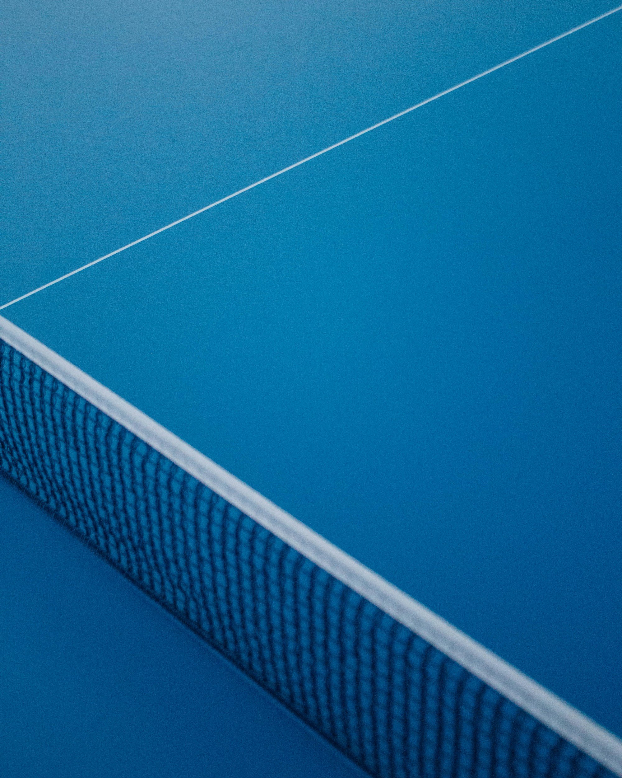 Close-up of a blue ping pong paddle and net on a blue ping pong table.