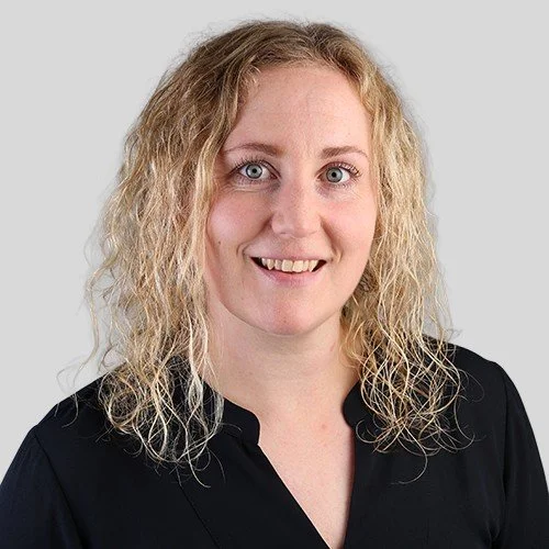 Portrett av en kvinne med blond, krøllete hår og blå øyne, iført sort skjorte.