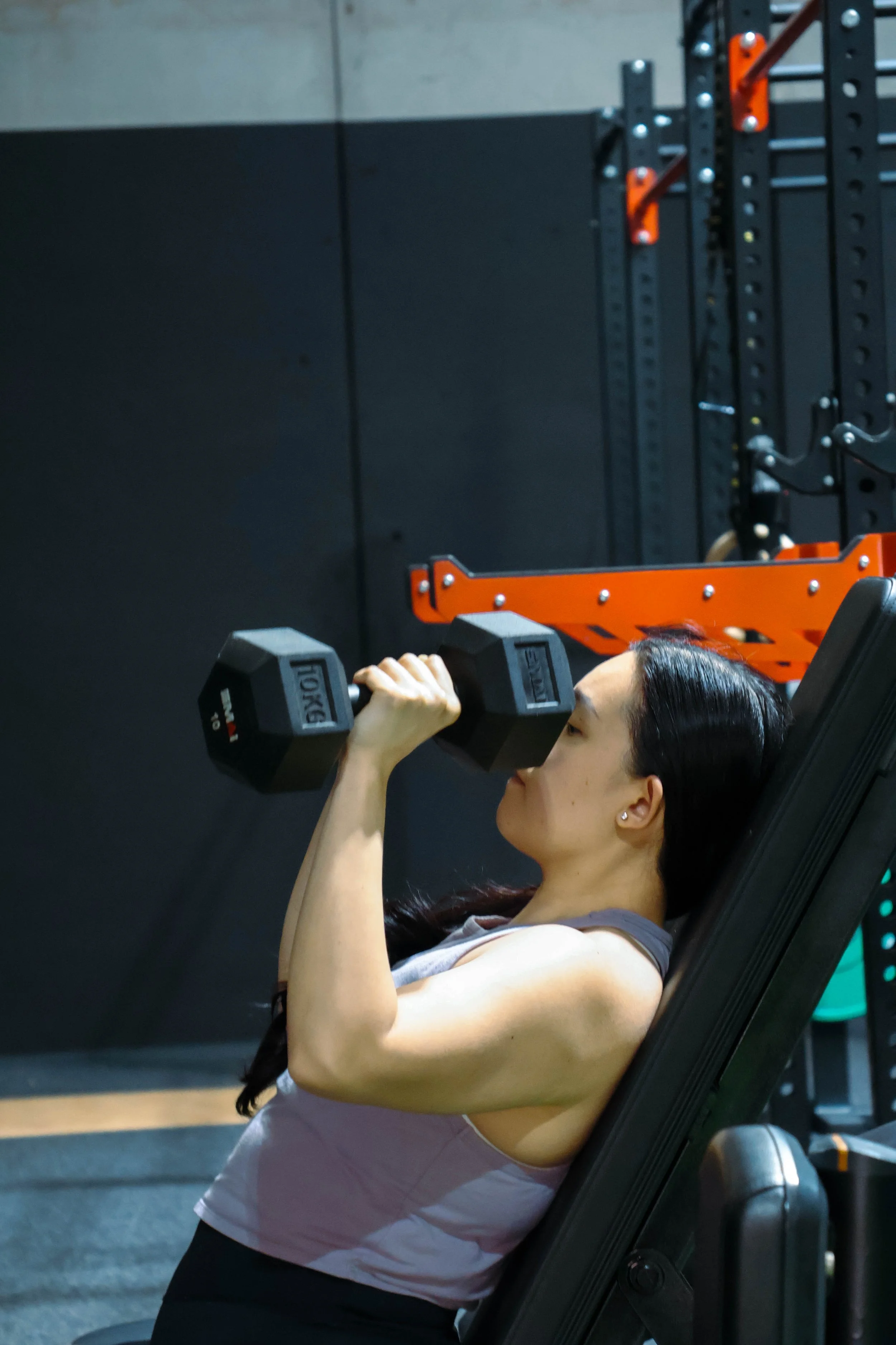 A woman lifting a dumbbell while seated on a workout machine in a gym.