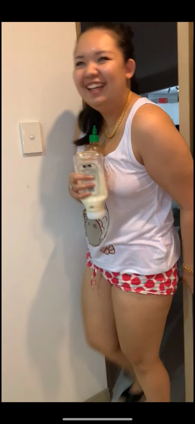 A woman laughing, holding a squeeze bottle of mayonnaise, wearing a white tank top and red polka dot shorts with a butterfly design.