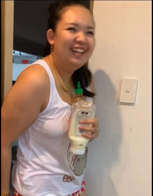 A woman smiling and holding a squeeze bottle of mayonnaise while standing indoors.