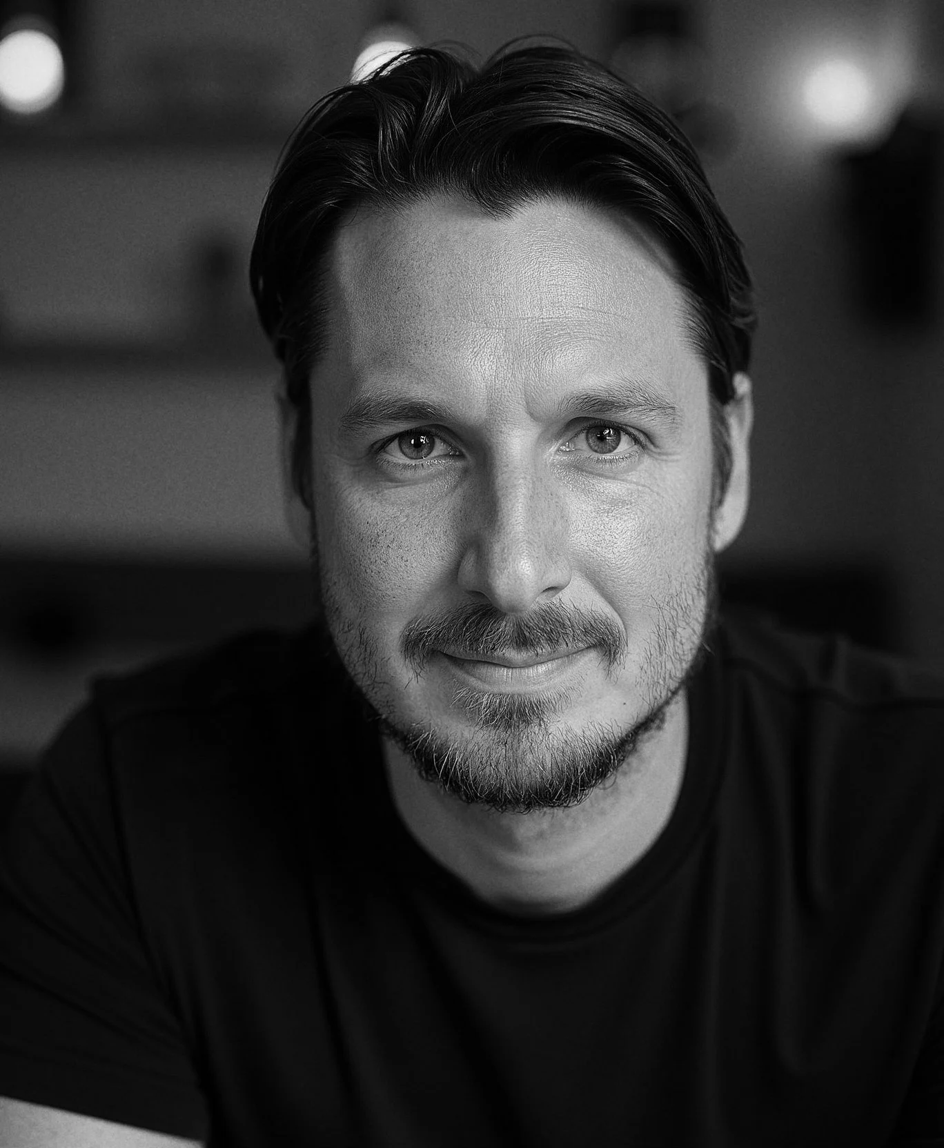 Hombre con barba y cabello oscuro, sonriendo y mirando a la cámara en un fondo borroso.
