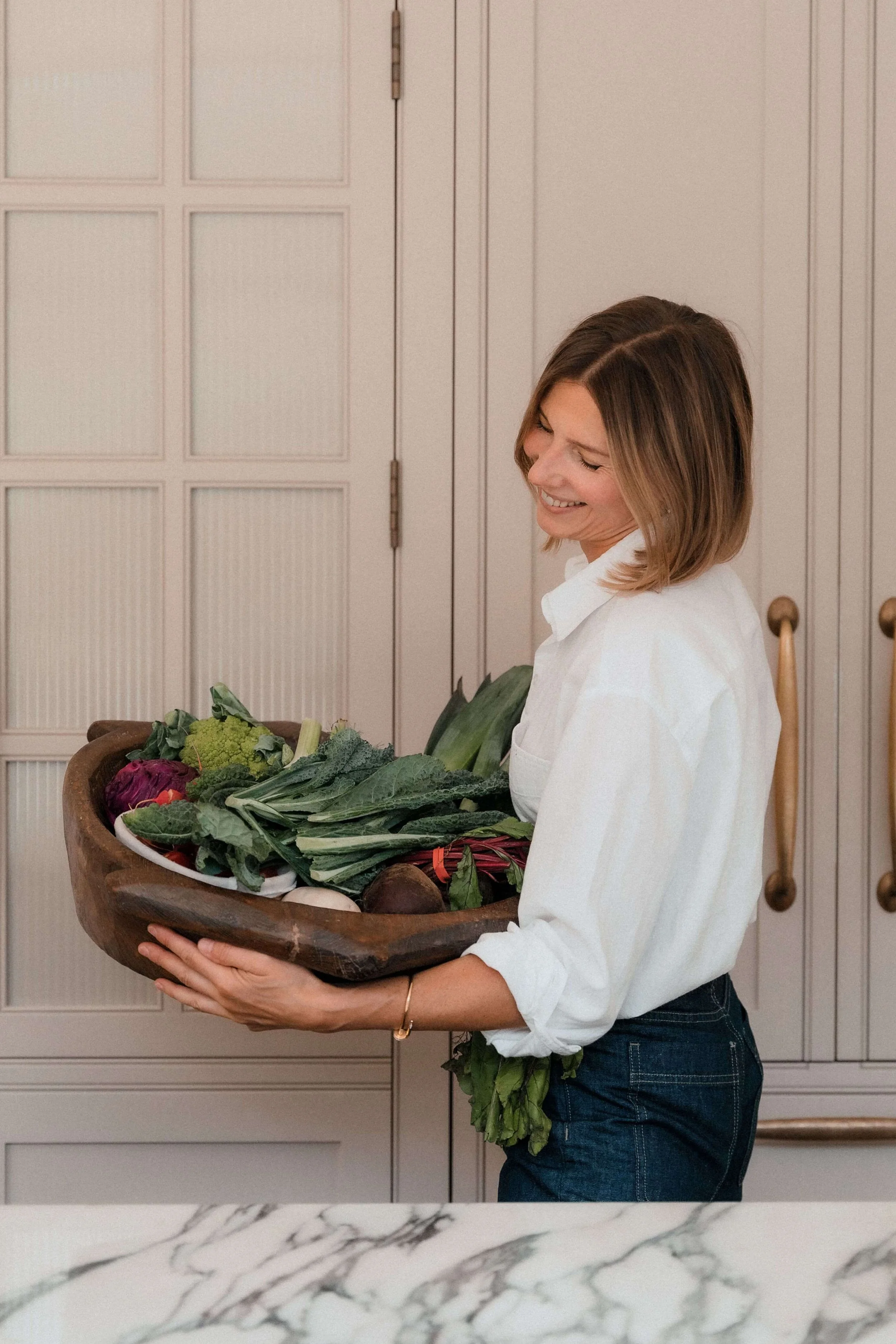 Nataliya Langhorne holding a bowl of fresh vegetables in her kitchen, menopause and acid reflux nutritionist supporting women with gut health