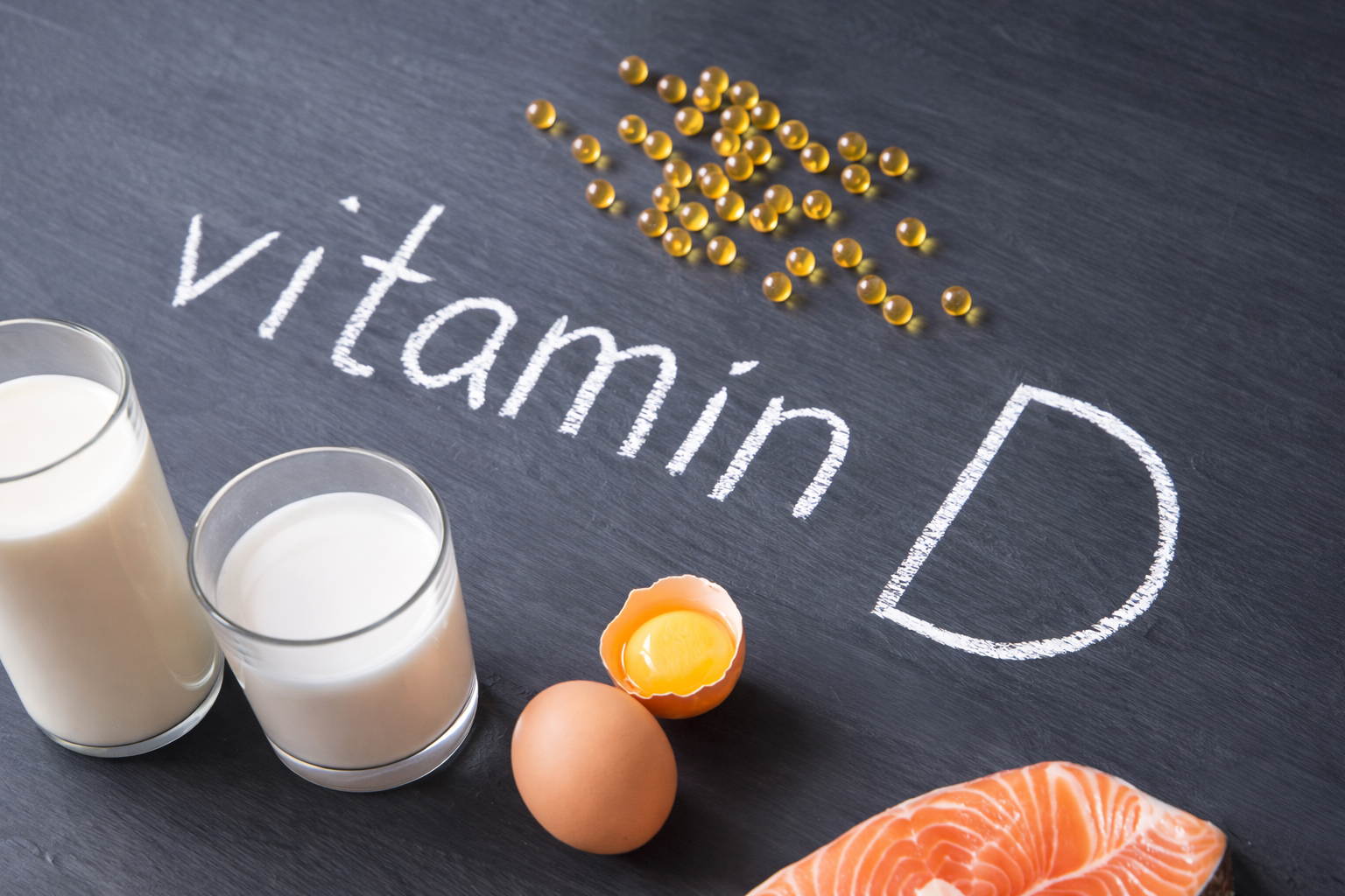 Vitamin D written on chalkboard with salmon and capsules, illustrating vitamin D supplements for perimenopause.