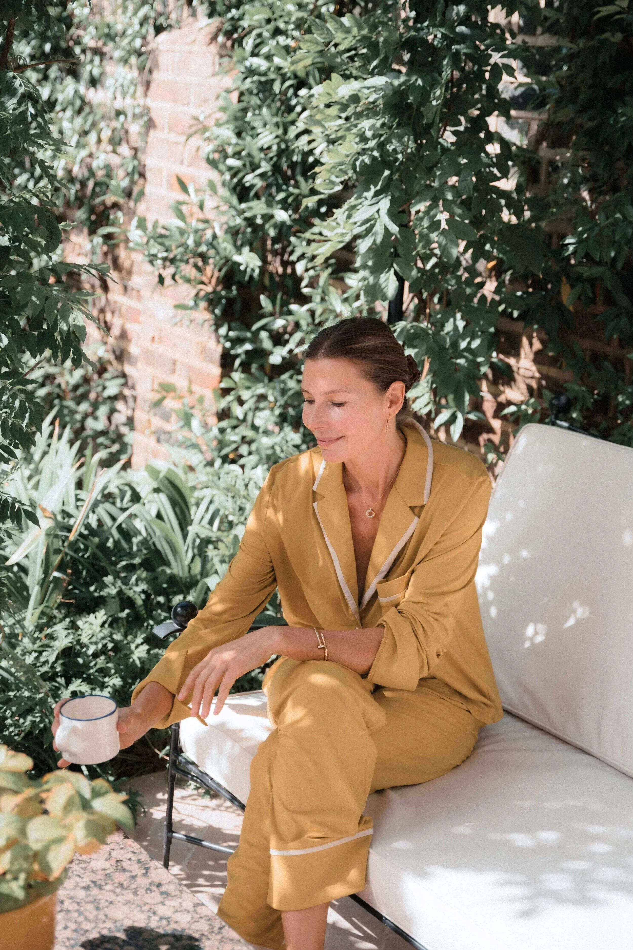 Midlife woman in pyjamas drinking coffee in the garden in the morning, feeling tired and dealing with menopause and acid reflux symptoms