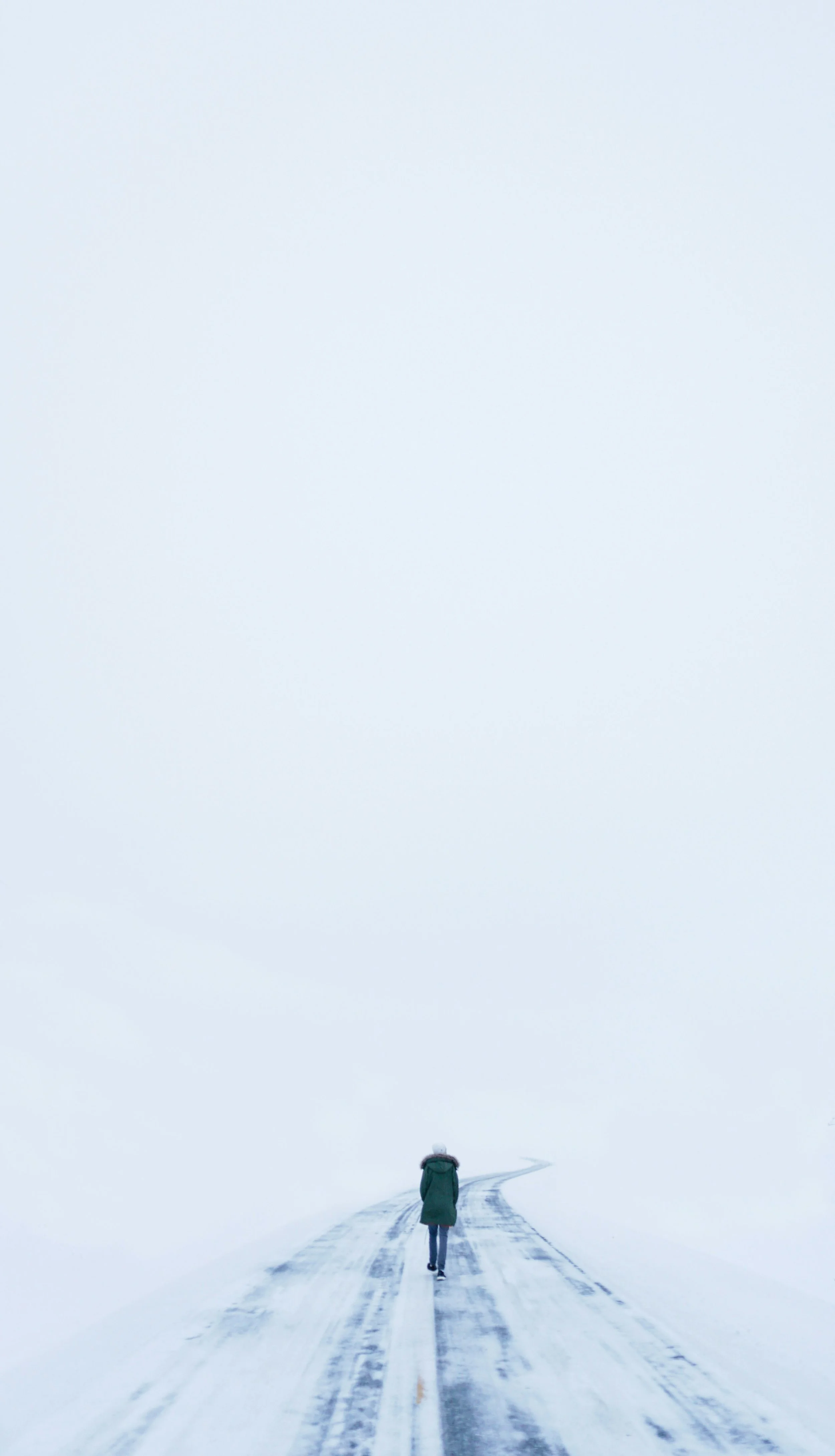 Person in einem Decken Mantel läuft auf einem Weg durch eine weiße Nebel-Schnee-Landschaft