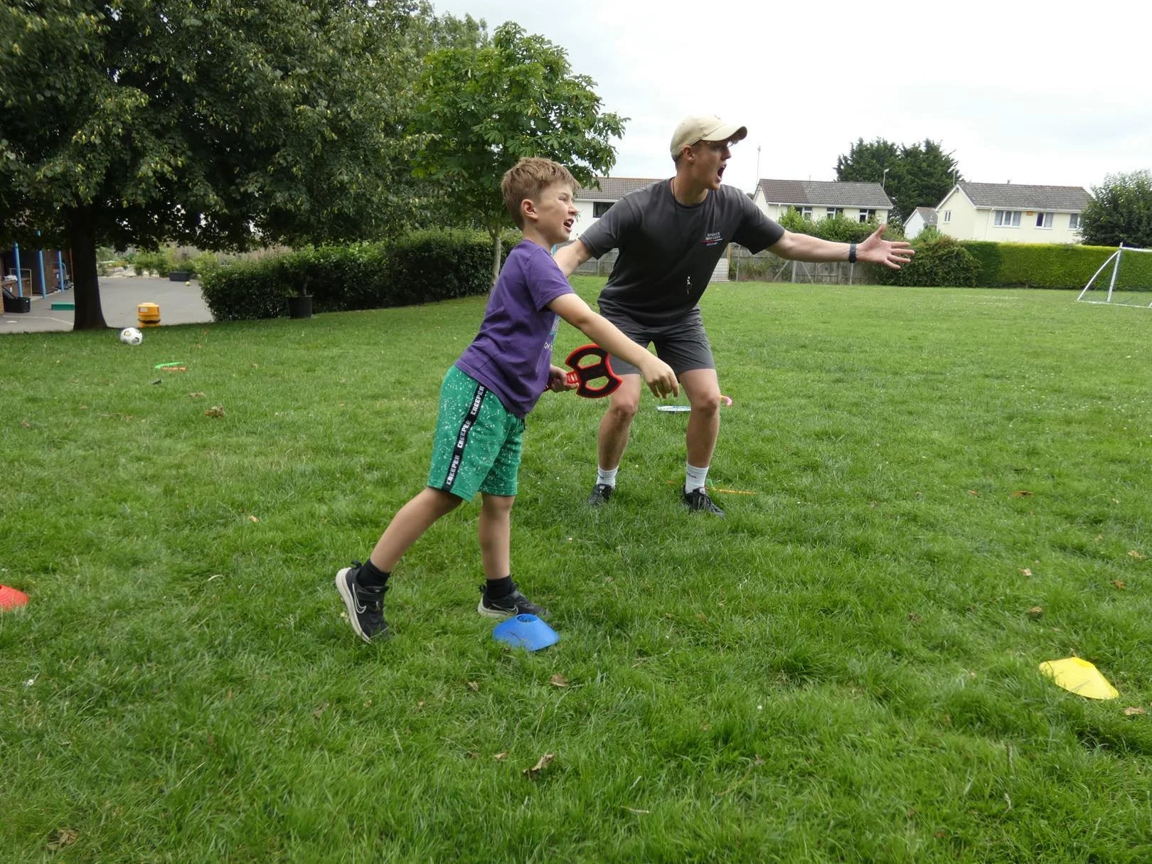 A young girl practicing rugby passing drills with a coach or trainer observing behind a wooden fence.