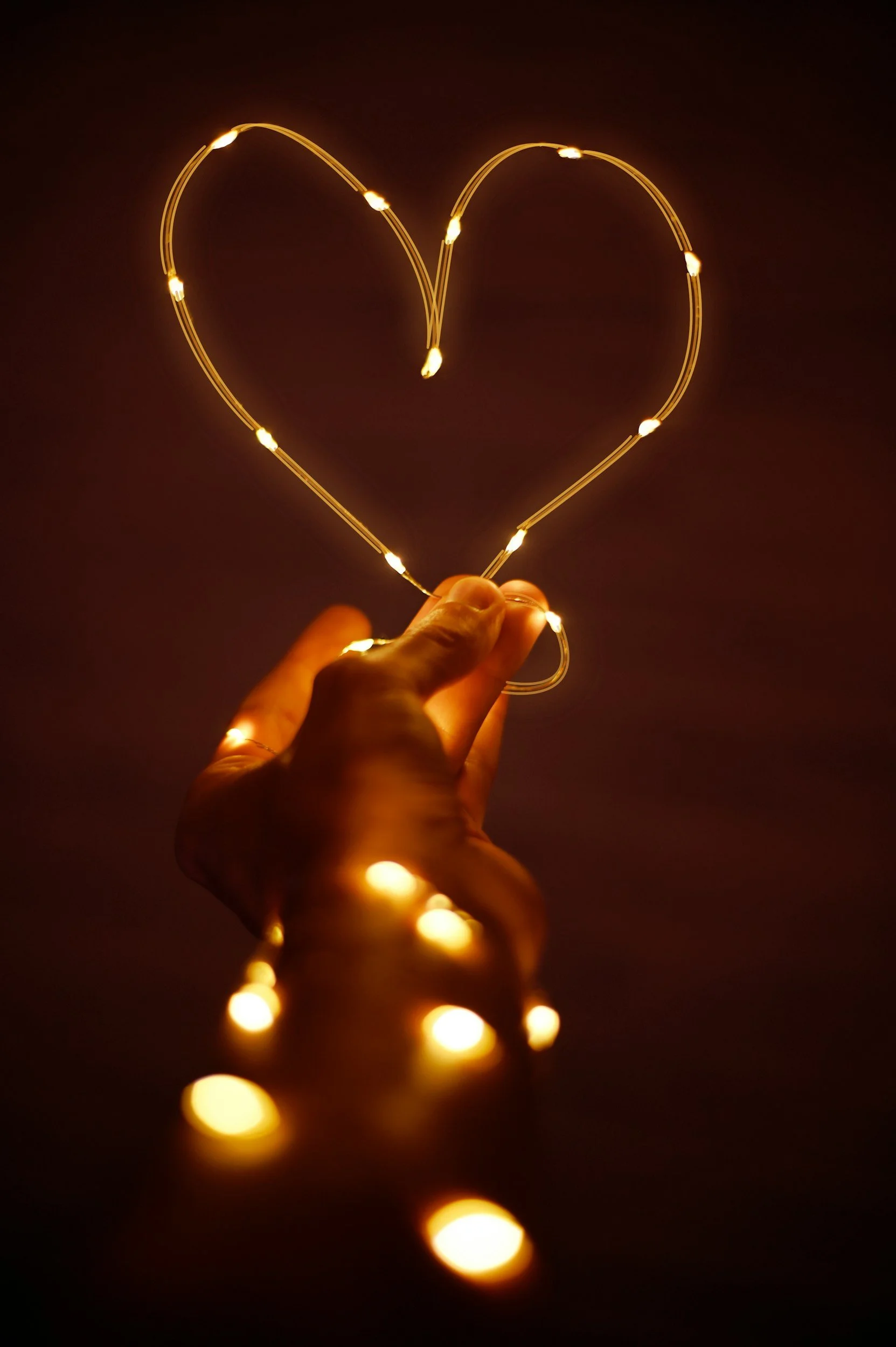 Hand holding a string of small, glowing lights that form a heart shape in the dark.