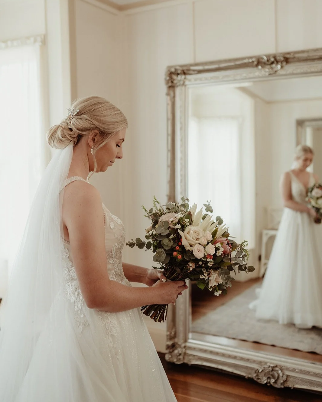 Bride holding a bouquet of flowers in a room with vintage mirror.