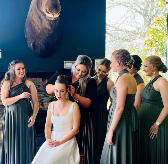 Bridesmaids helping a bride with her hair and makeup before her wedding in a decorated room with a mounted animal head on the wall.