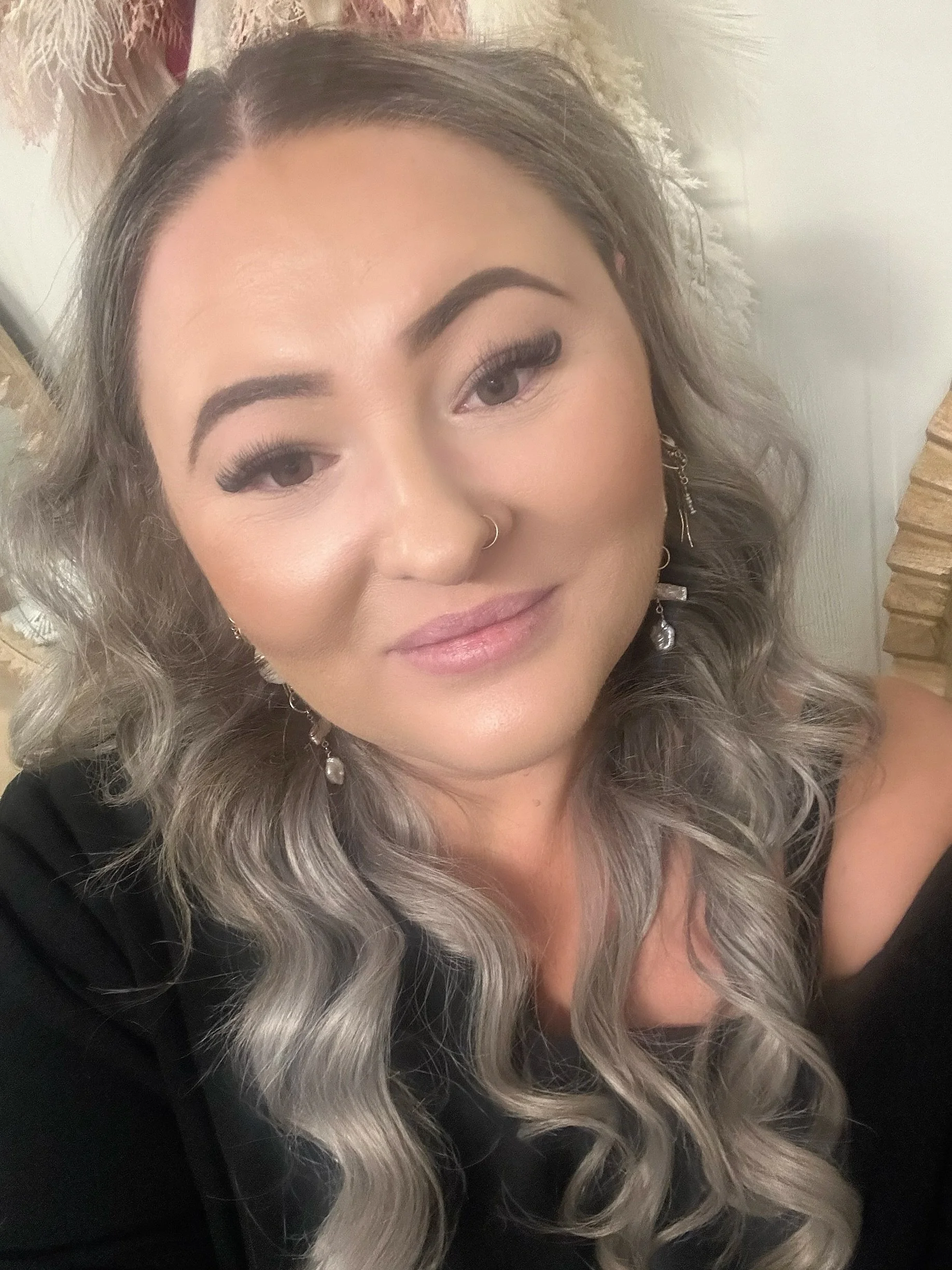 Close-up of a woman with long, curly gray hair, wearing earrings and a black top, smiling slightly.