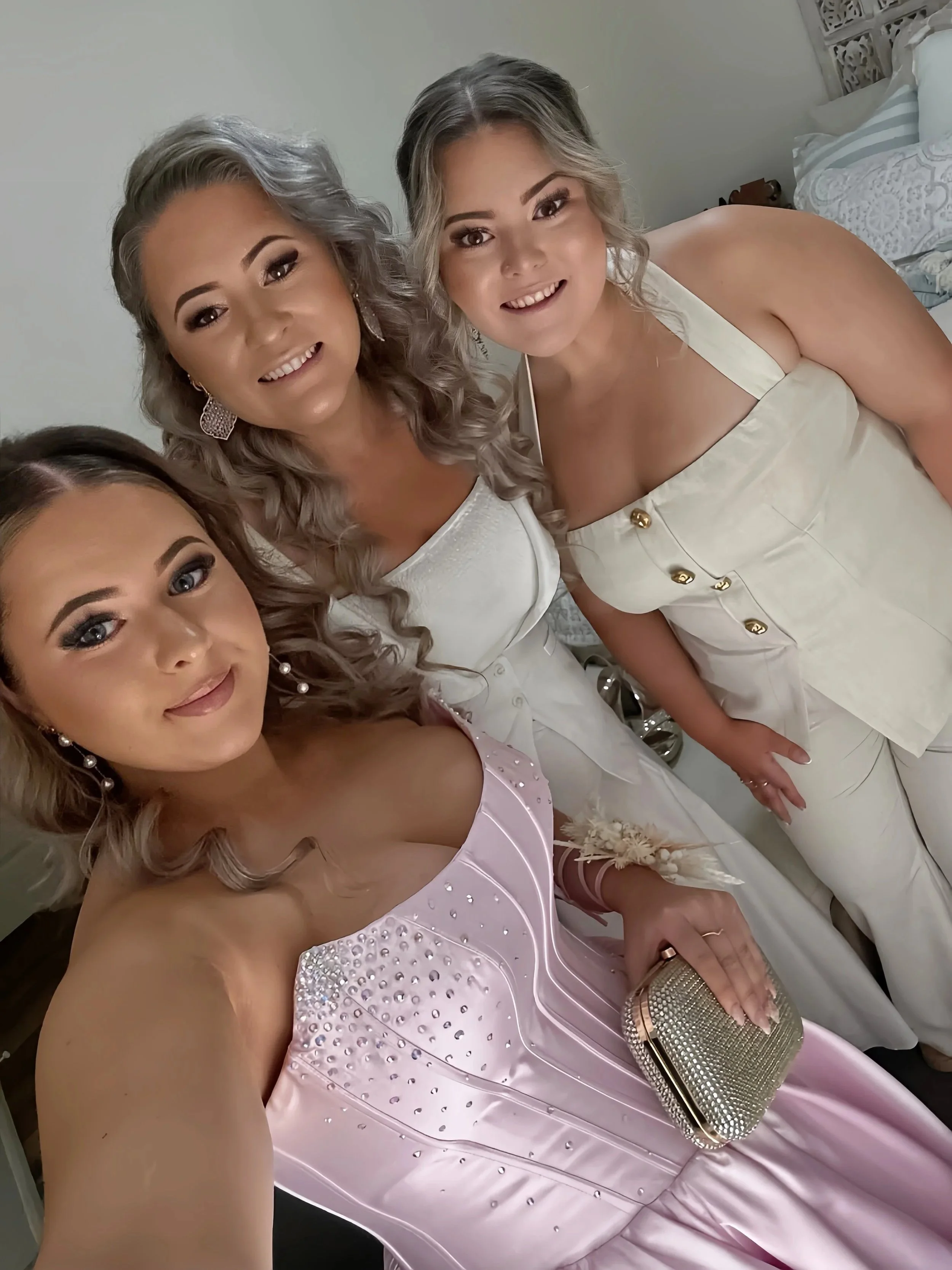 Three women dressed in elegant gowns taking a selfie together at a formal event.