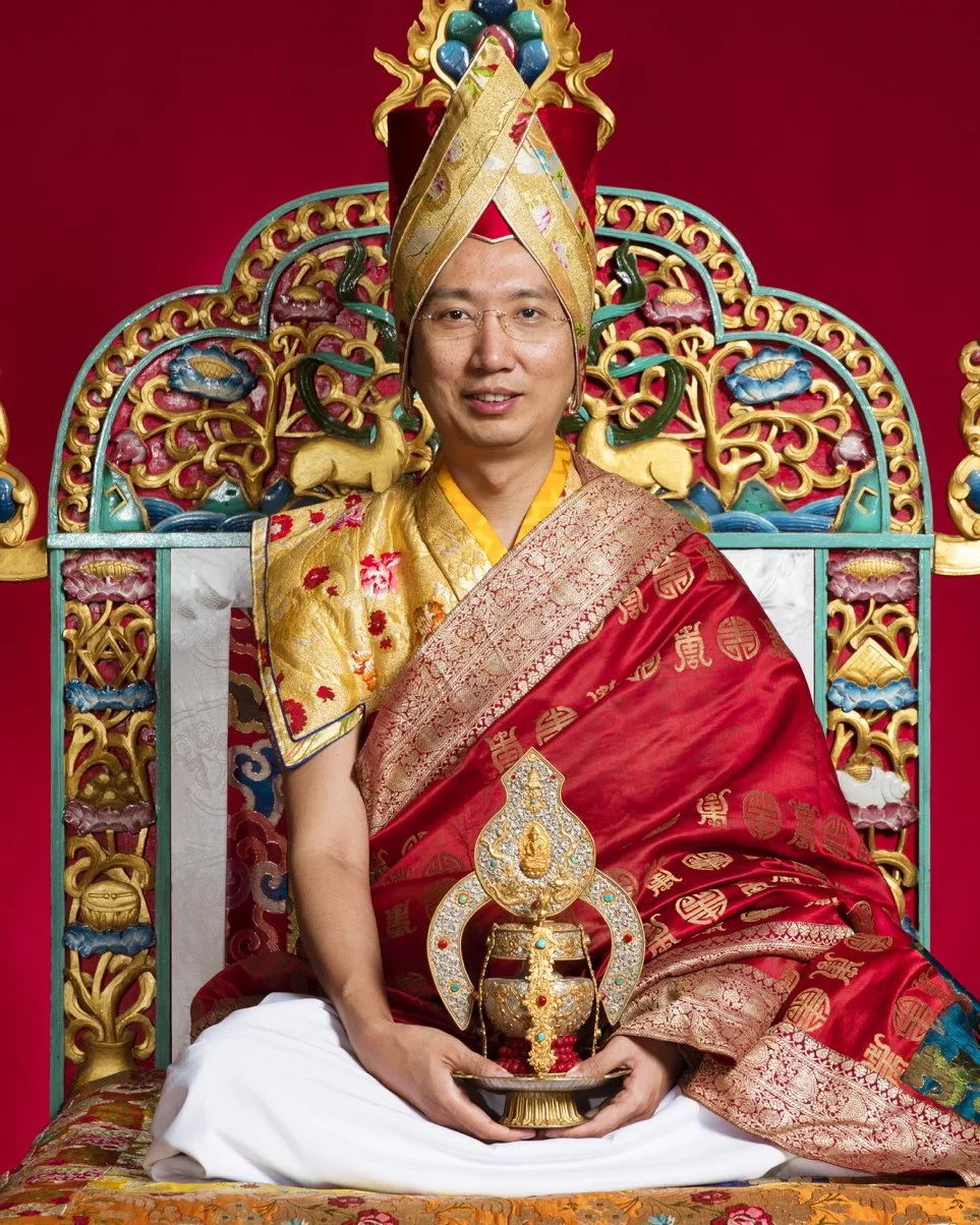 Man dressed in traditional Thai royal attire, seated on an ornate throne with colorful decorations and intricate patterns.