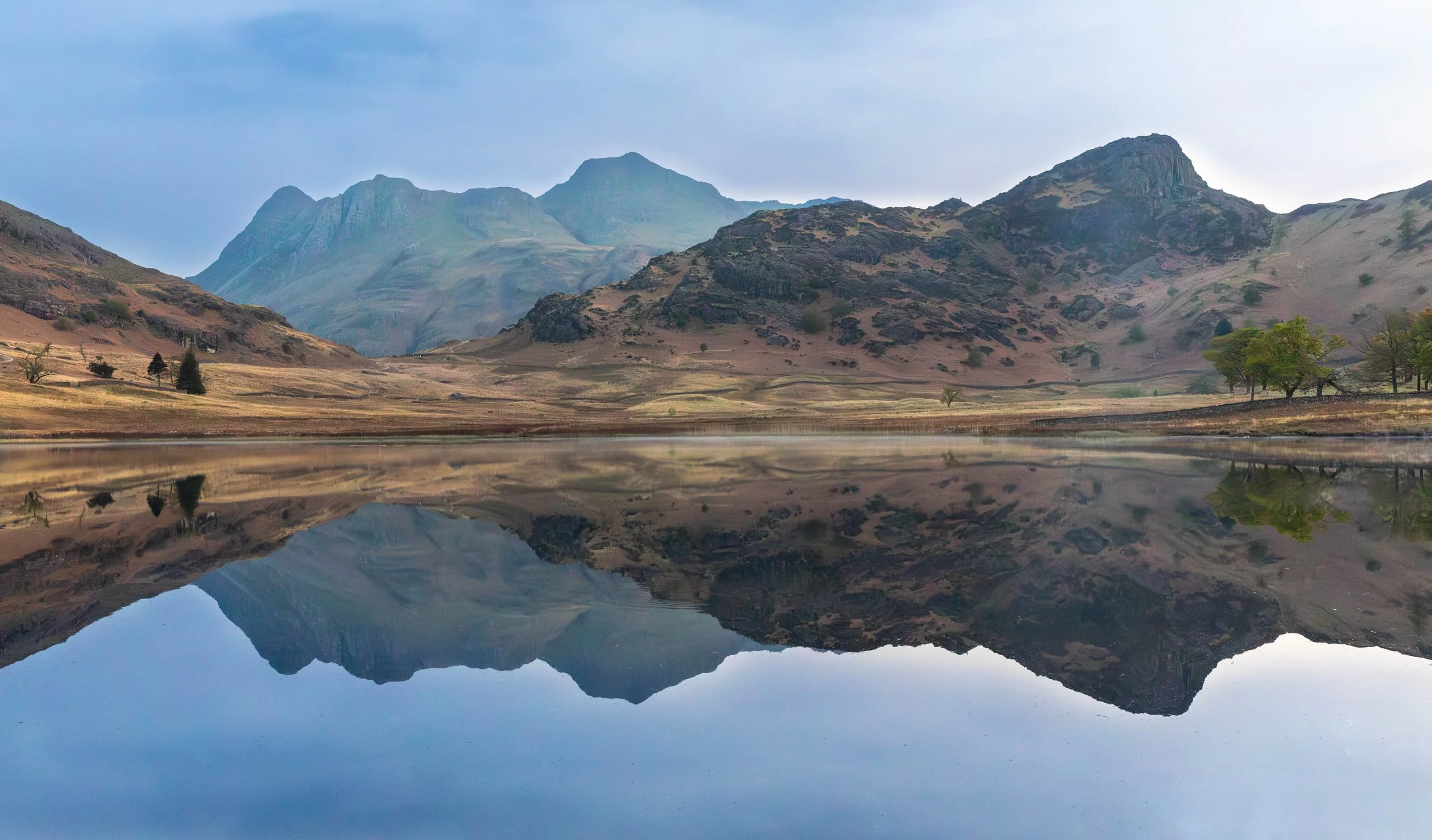 Scenic landscape of mountains reflected in a calm lake with a few trees on the shoreline.