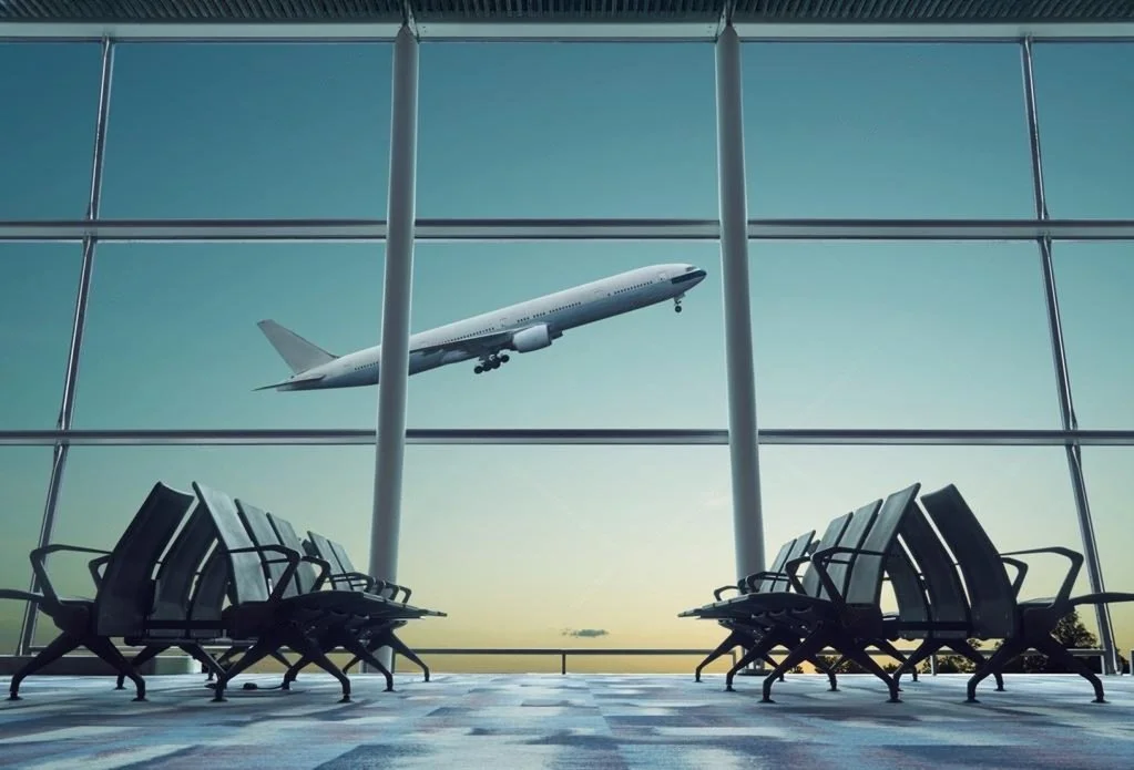 An airplane flying outside a large airport terminal window with empty seating inside.