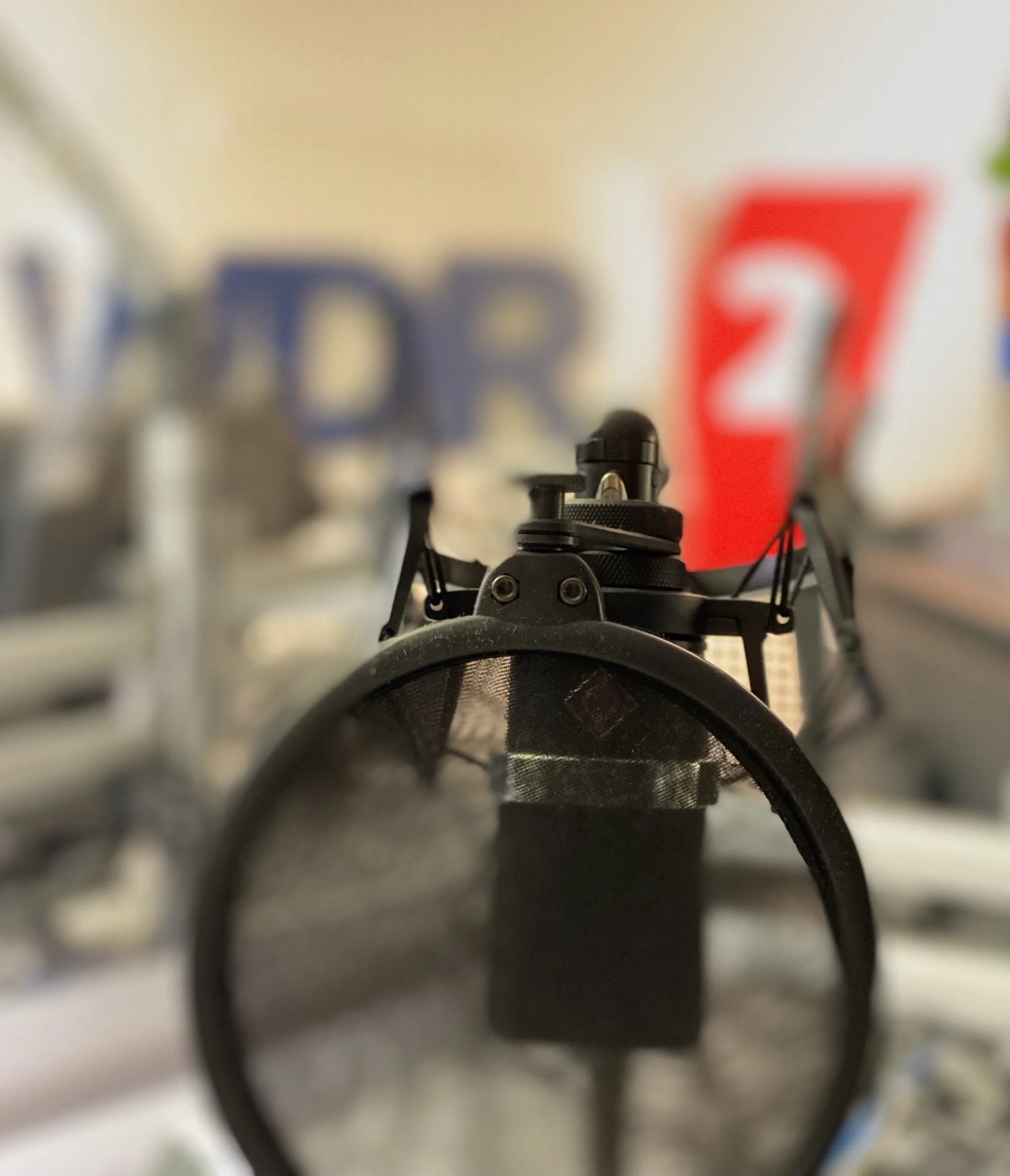 Nahaufnahme eines Mikrofons mit einem Schaufenster im Hintergrund, auf dem die Buchstaben 'WDR' und die Zahl '2
' sichtbar sind.