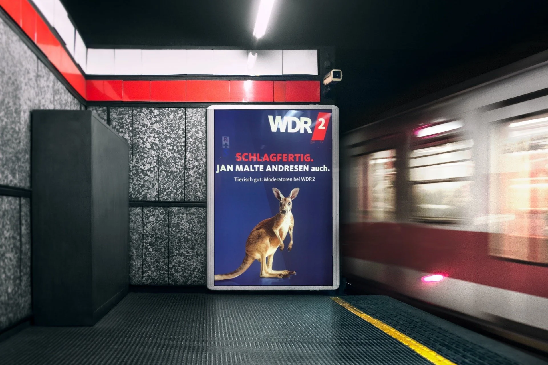 U-Bahn-Station mit Werbetafel für WDR 2, zeigt ein Tier mit der Überschrift ‚SCHLAGFERTIG.‘ und die Angabe, dass Jan Malte Andresen Moderator ist. Im Hintergrund fährt eine U-Bahn, die schnell vorbeifährt.