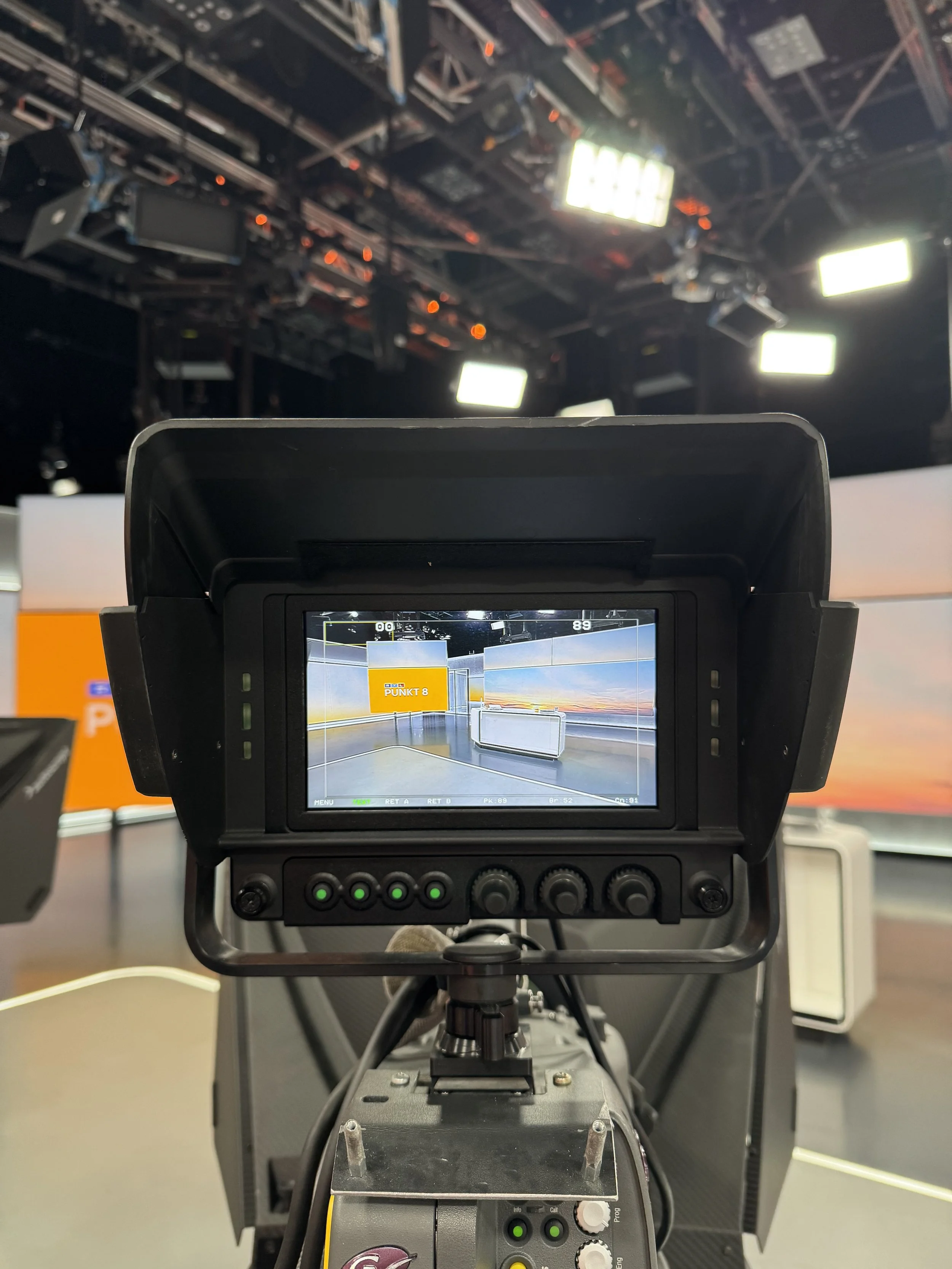 Blick durch die Kamera auf ein Fernsehintstudio mit Kameratechnik, Studiobeleuchtung und LED-Wand im Hintergrund.