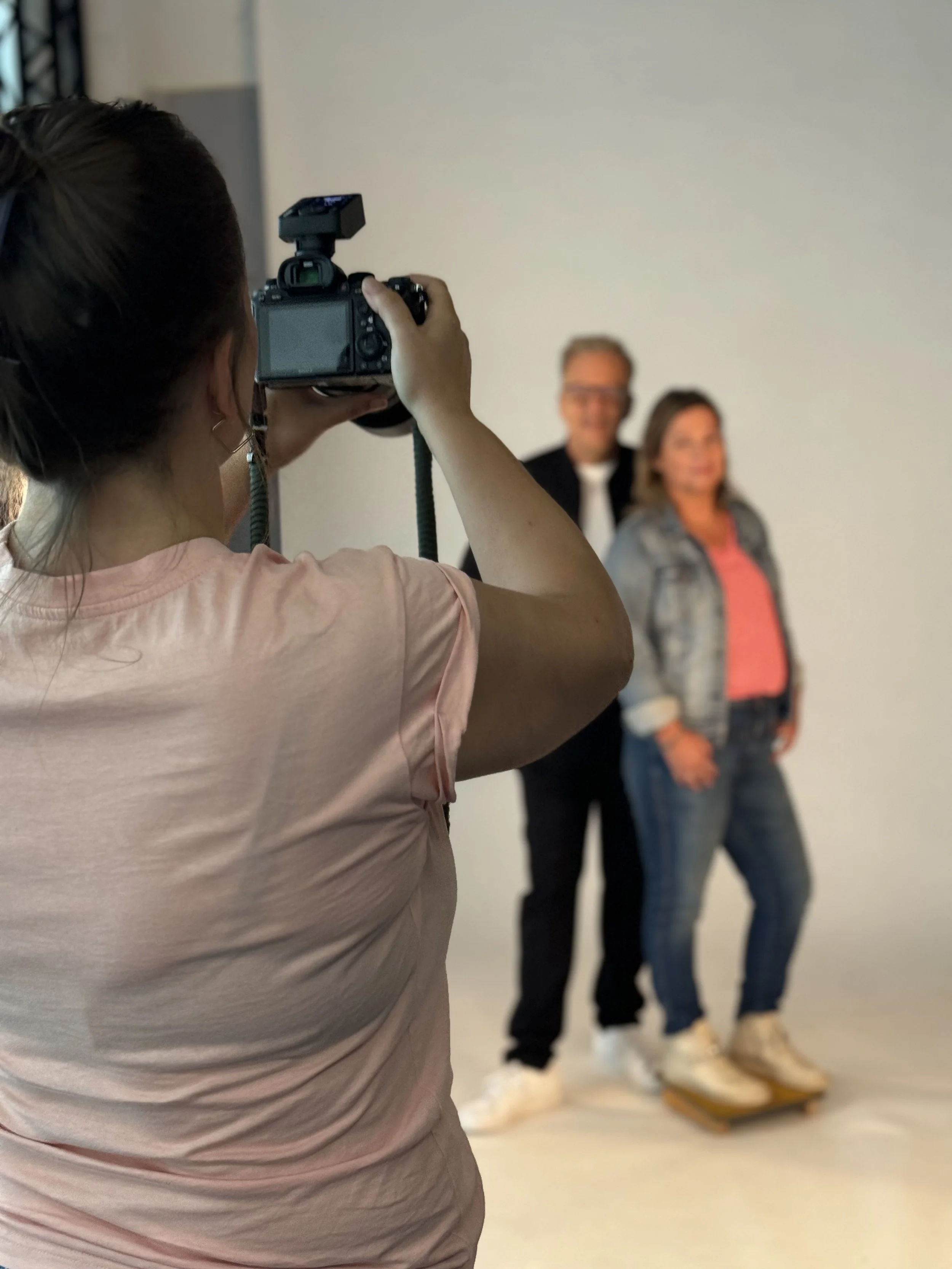 Fotografin macht ein Foto von einem Mann und einer Frau, die auf einem Balanceboard stehen, vor einem weißen Hintergrund.