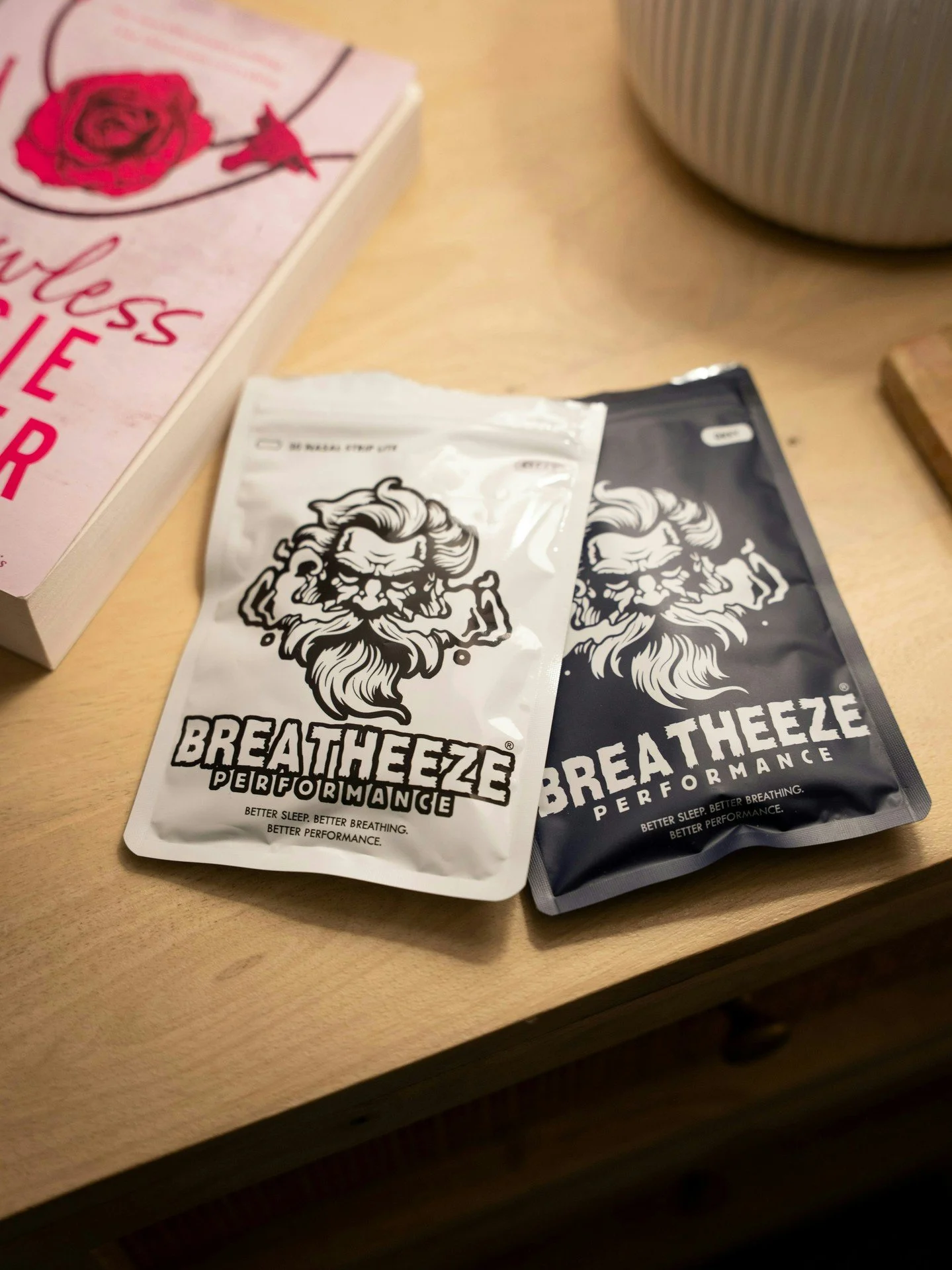 Packets of BreatheEzee performance breathing strips, one in white and one in black, placed on a wooden surface.