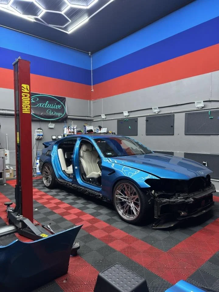 A partially assembled blue sports car in a workshop with colored walls, advanced lighting, and automotive equipment.