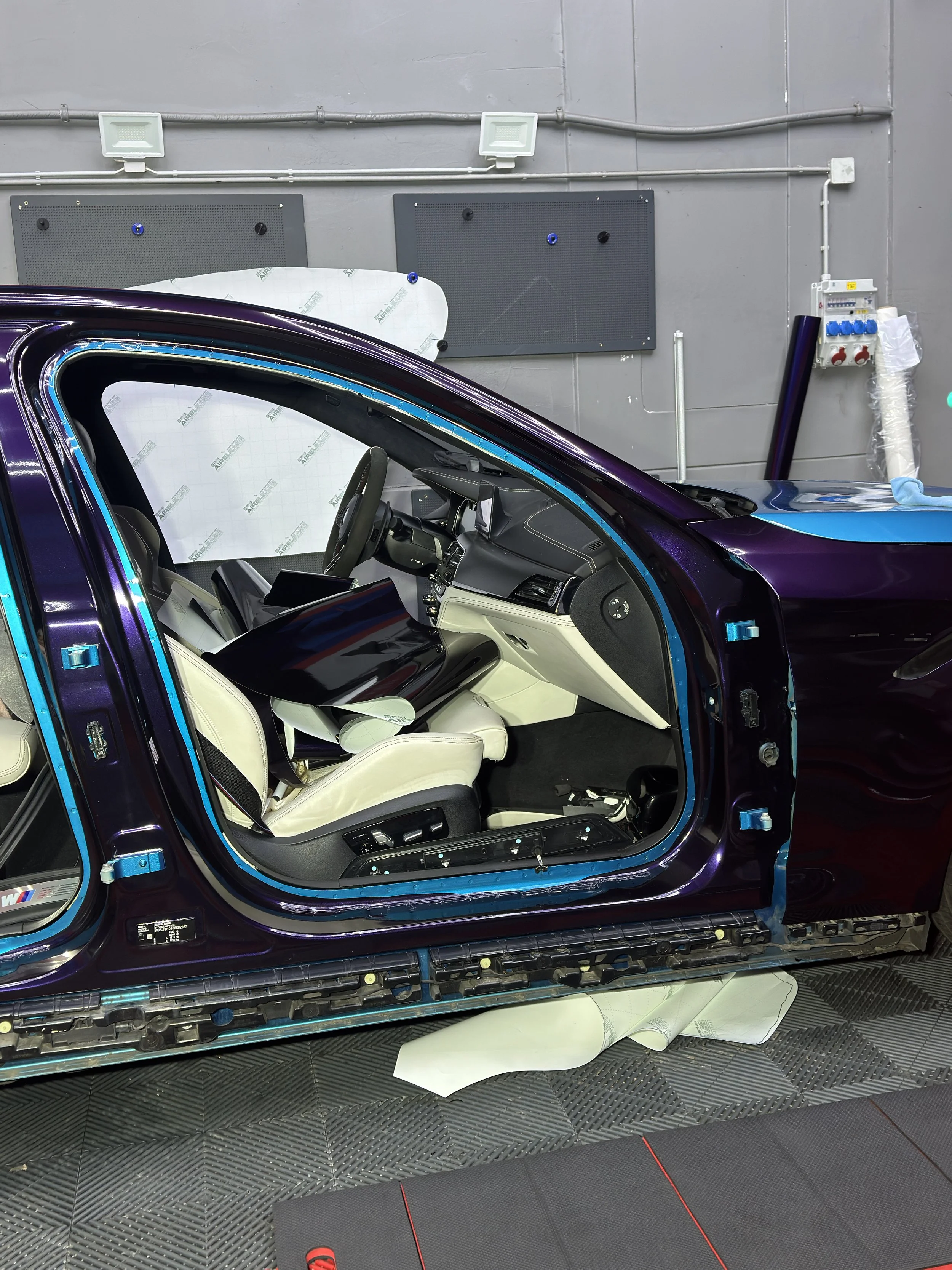 Interior of a car undergoing assembly or repair, with the car door open and various tools and components visible.